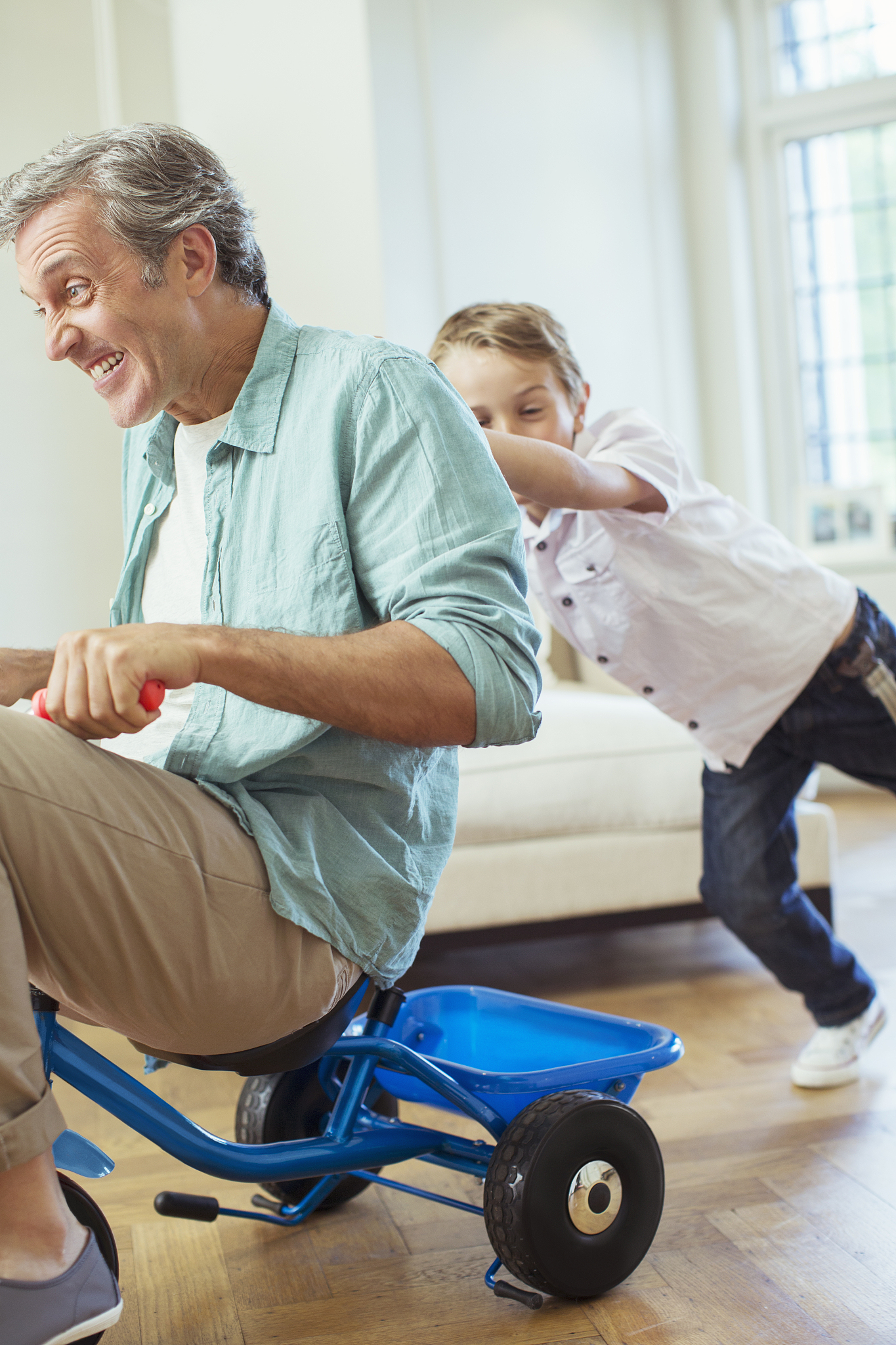boy pushing father on tricycle indoors