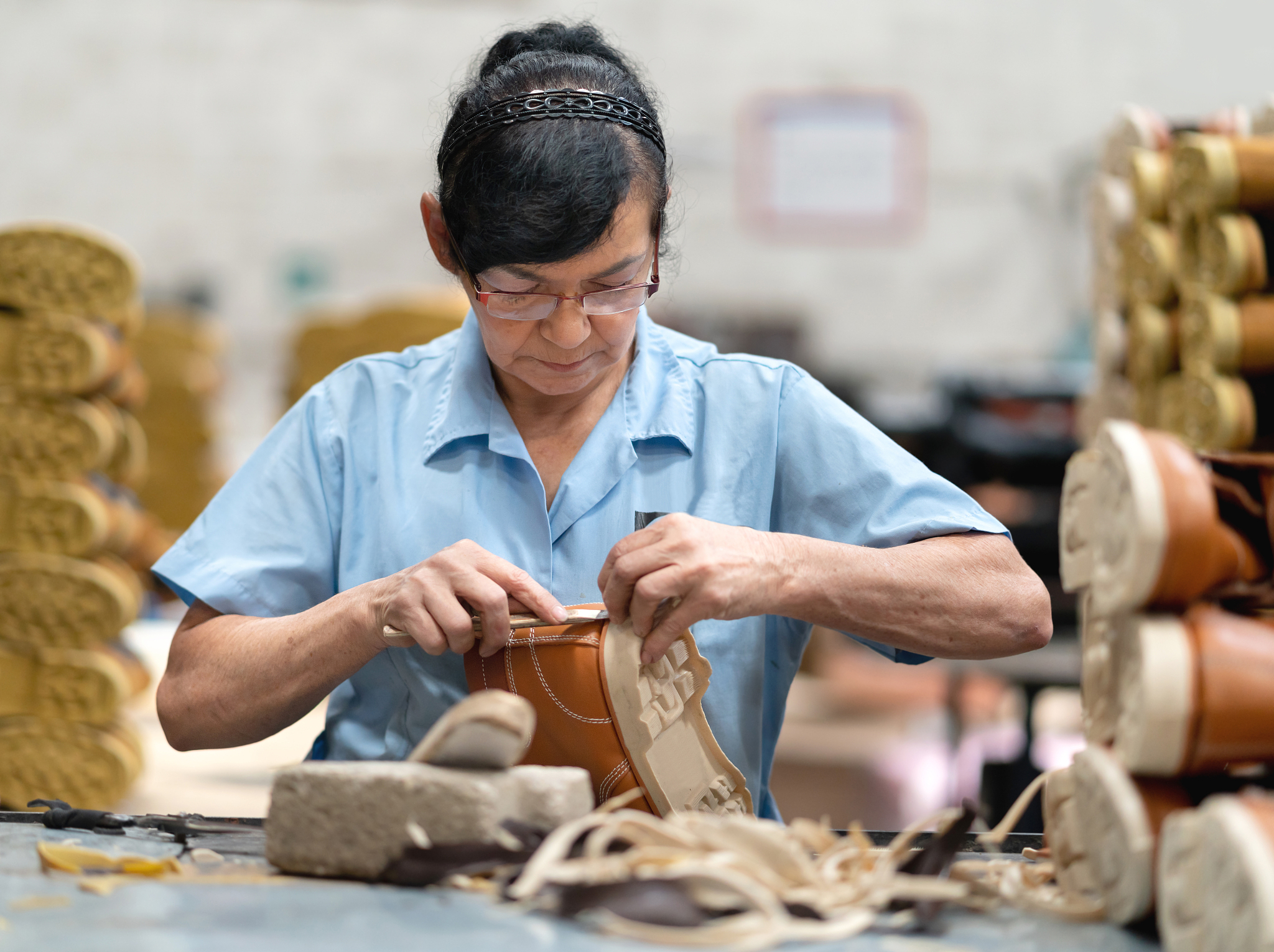 adult female cobbler cutting excess rubber from sole shoe