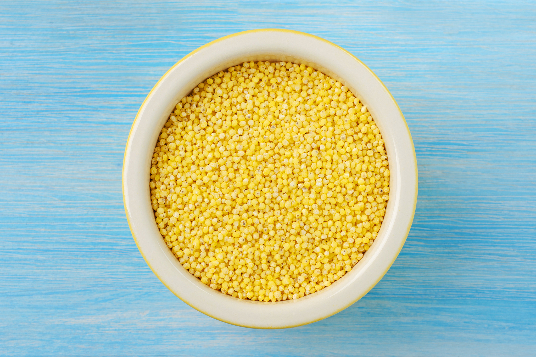organic millet seeds in a ceramic bowl on wooden blue rustic bac