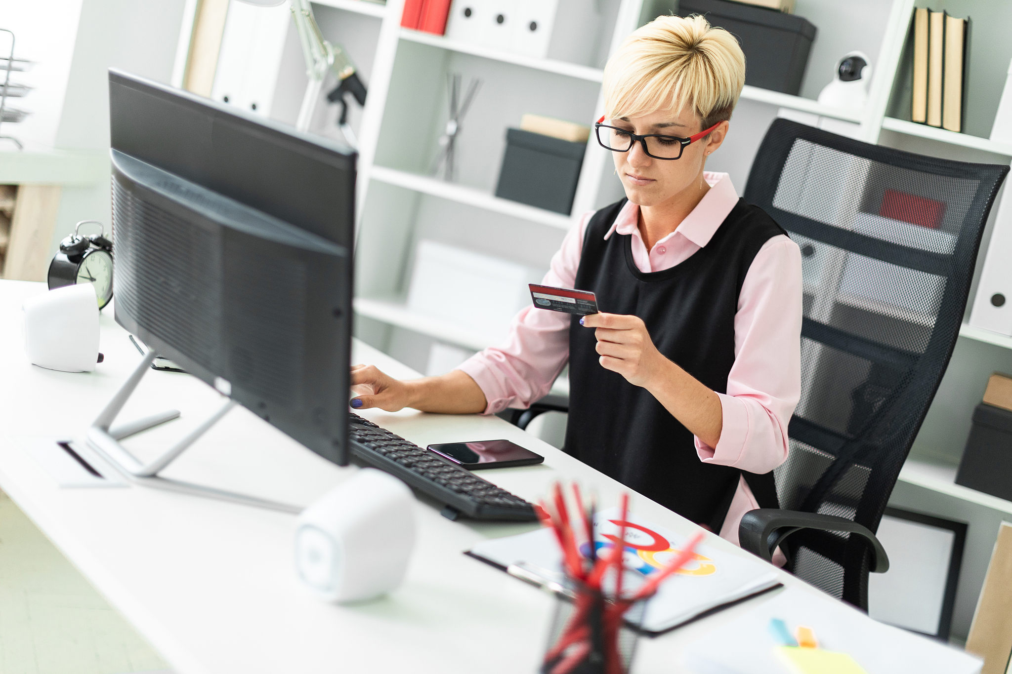 a young girl sitting at a computer table and holding a bank card