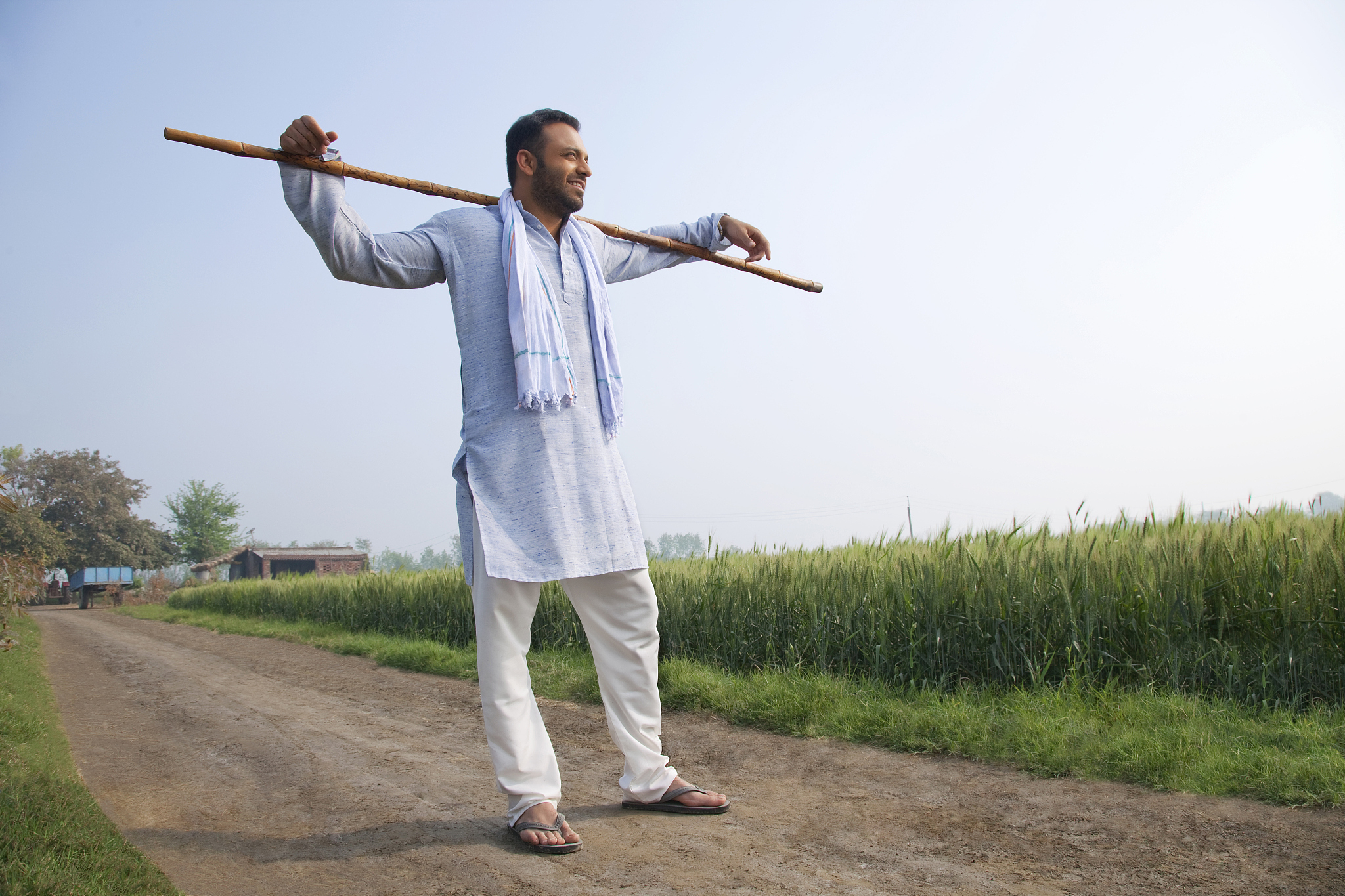 full length of an indian man standing with a stick across his sh