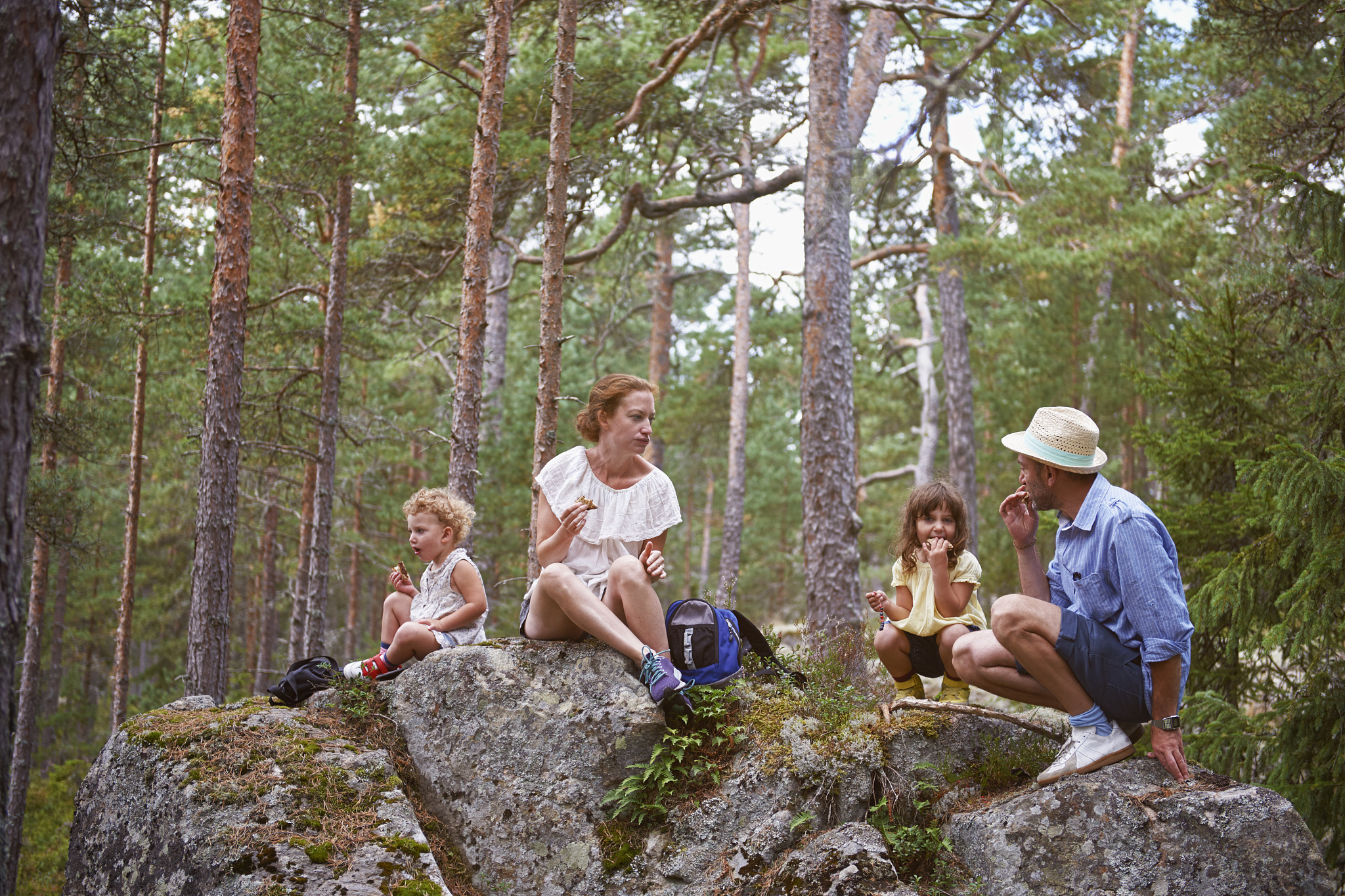 family sitting on rocks in forest eating picnic
