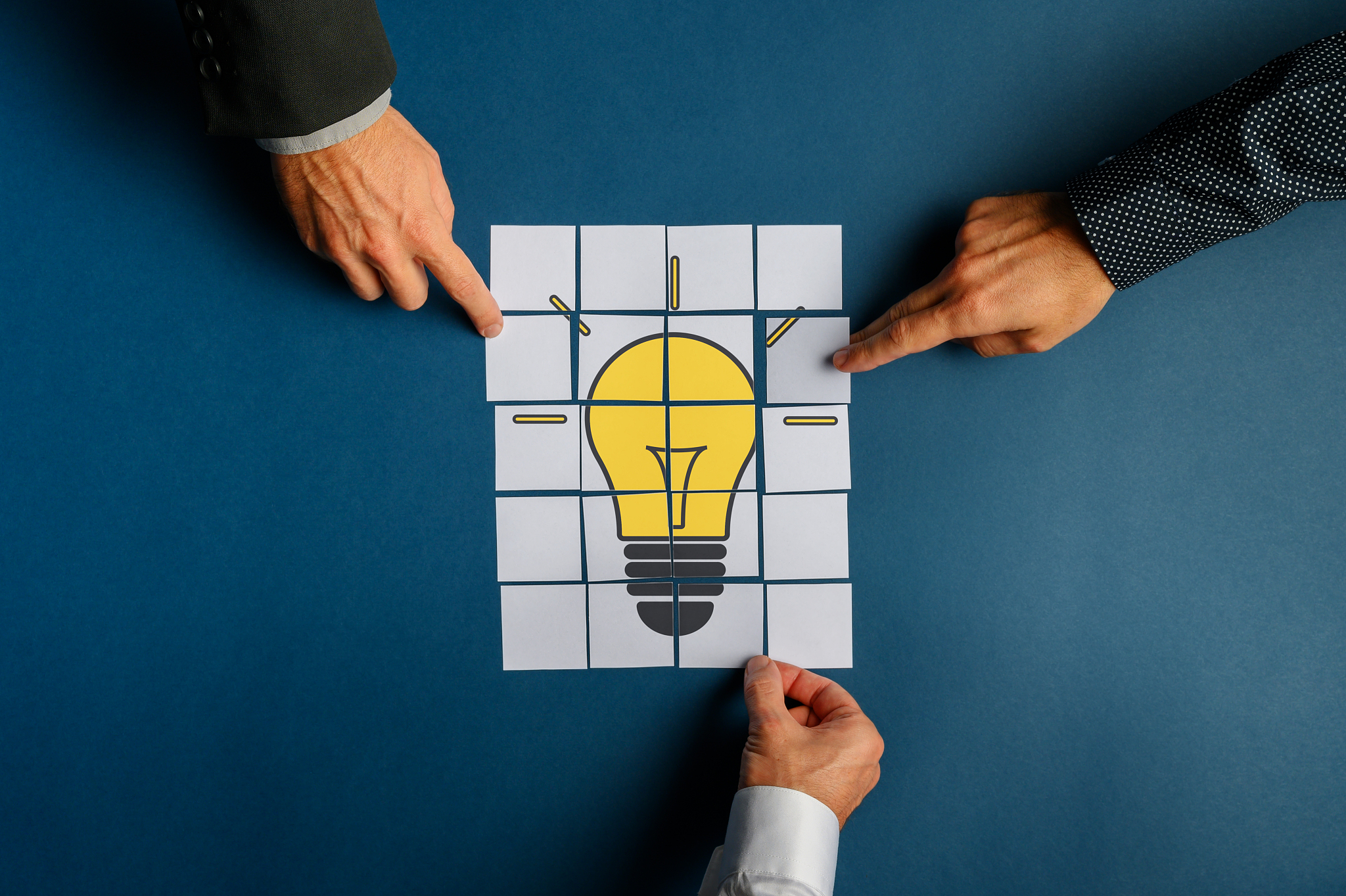 hands of three businessmen assembling a lightbulb drawn on post 