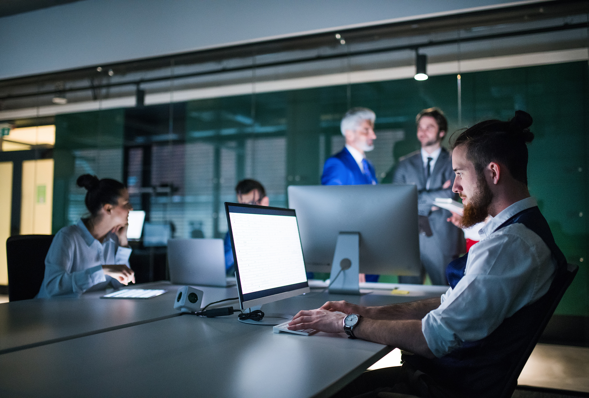 a group of business people in an office at night, using computer