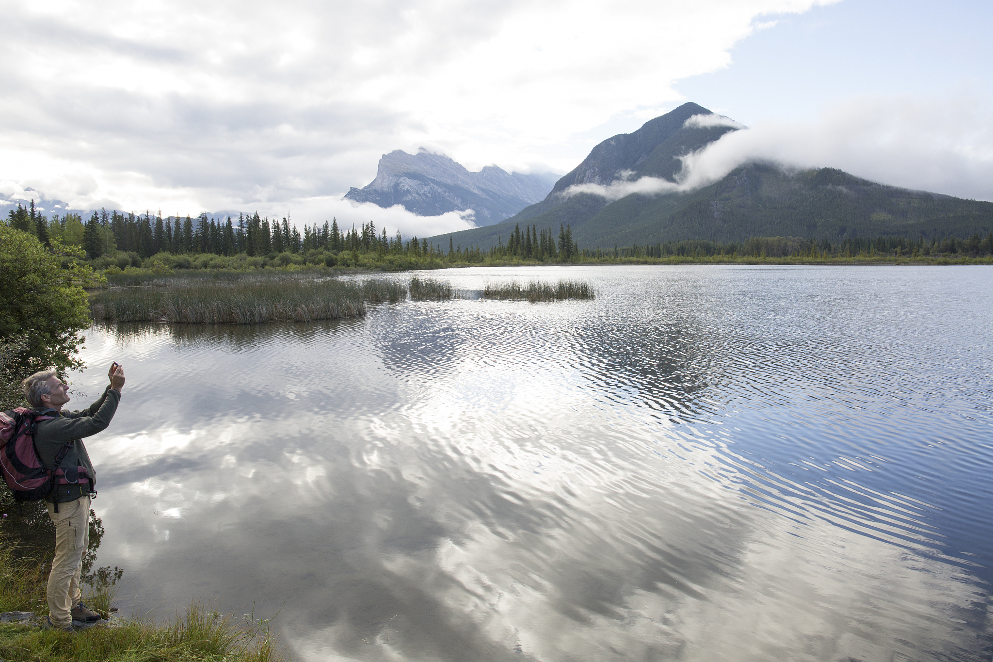 male hiker takes pic by mountain lake edge