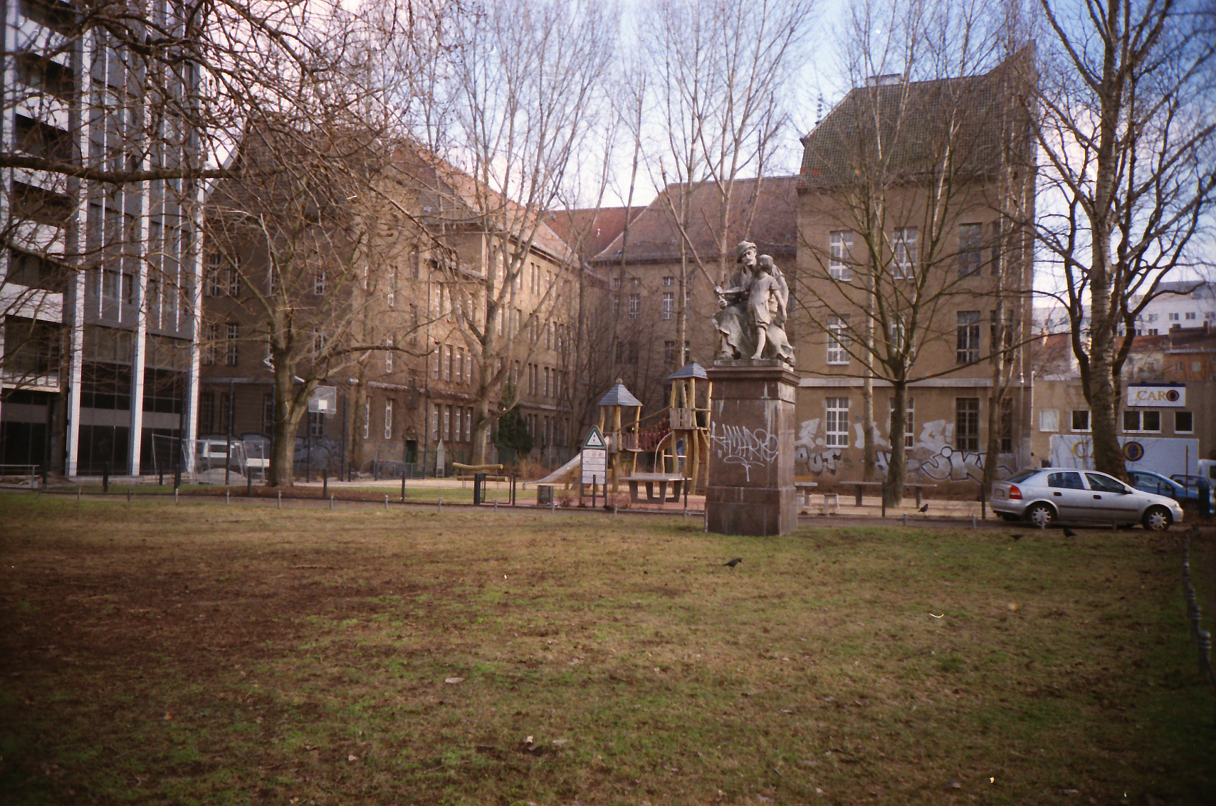 a statue stands in a park between a playground and a building