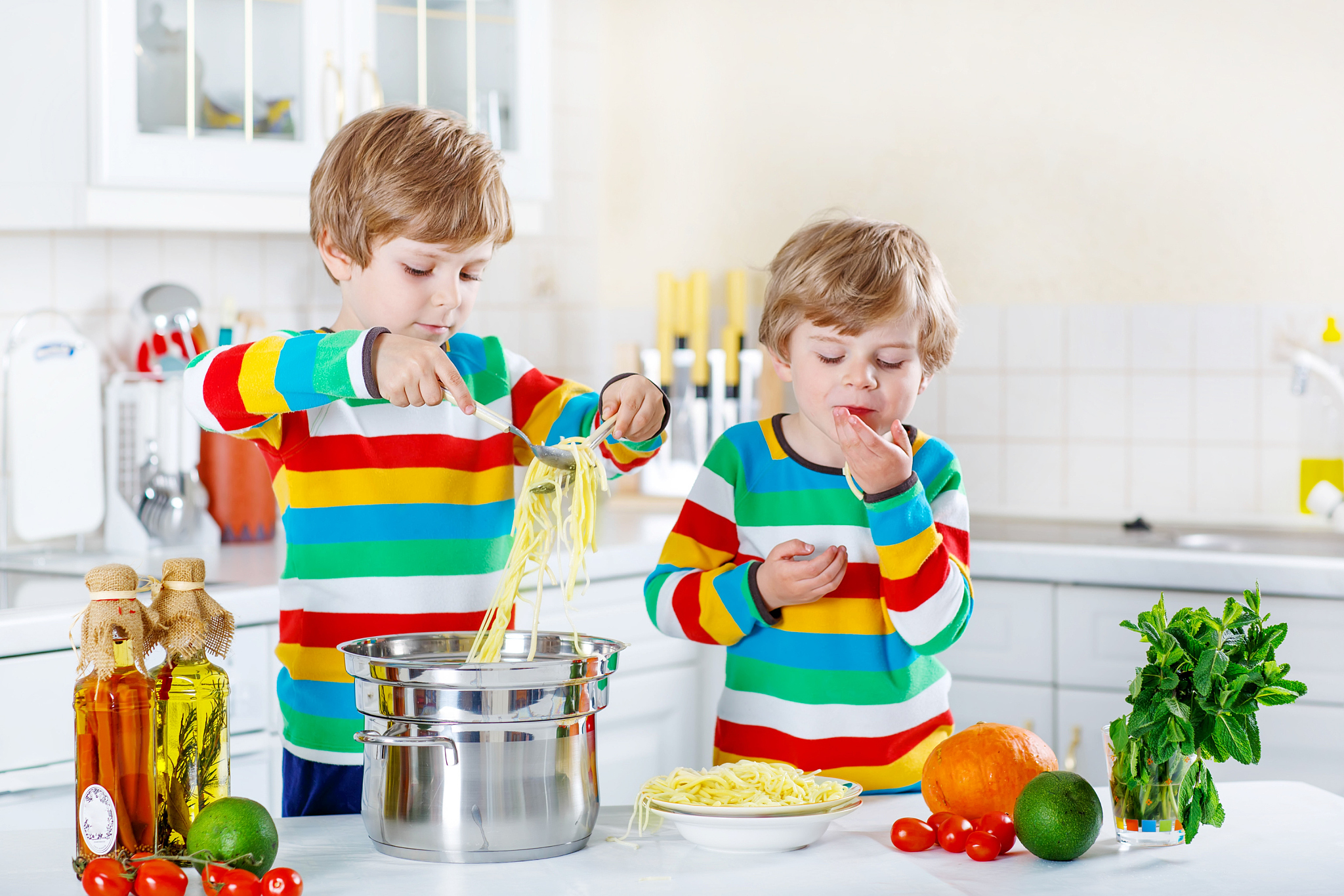 two little kid boys eating spaghetti in domestic kitchen.