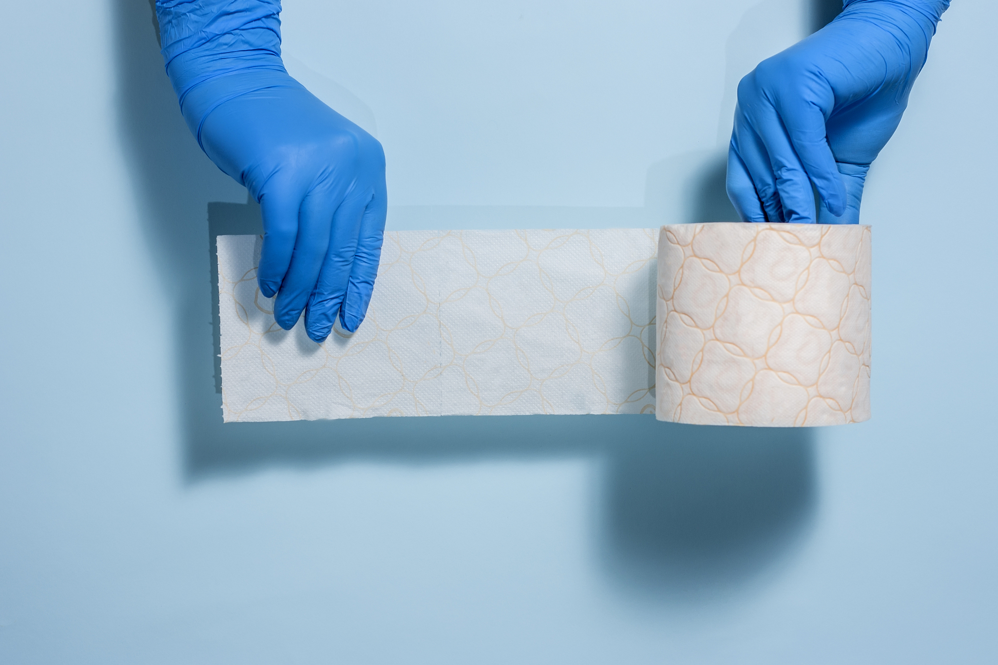 two hands in sterile rubber gloves hold a roll of toilet paper o