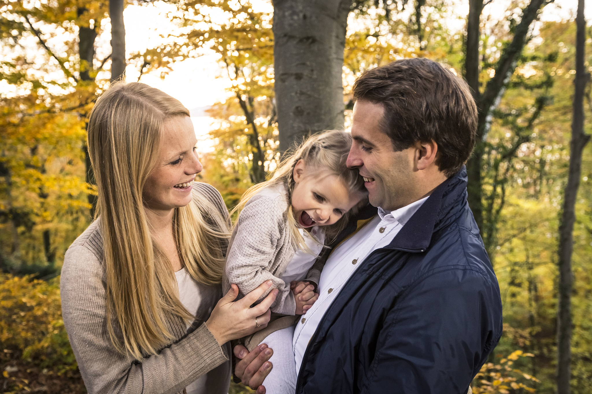 smiling woman standing by man carrying cheerful daughter in fore