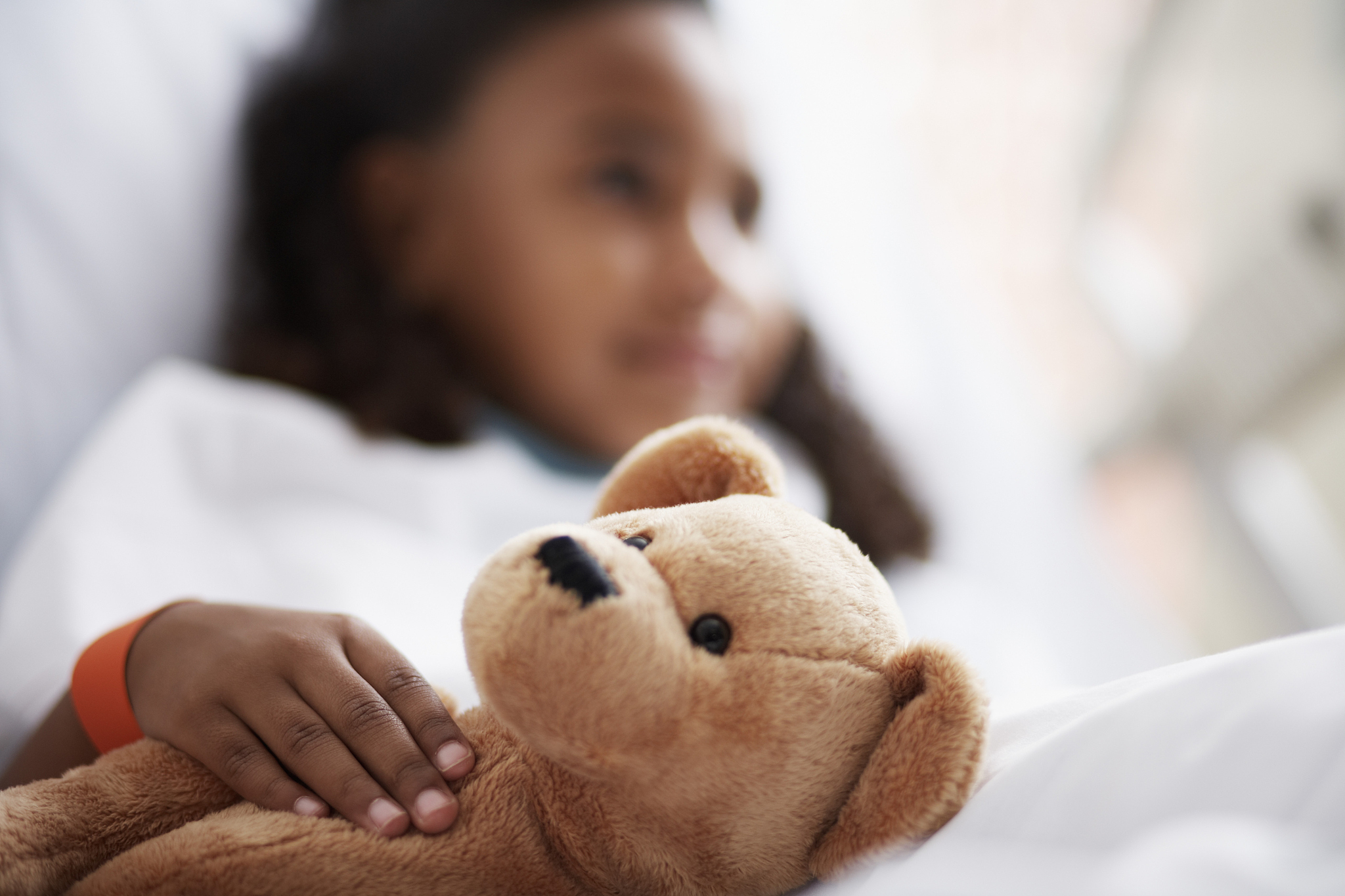 little girl with teddy bear in hospital bed