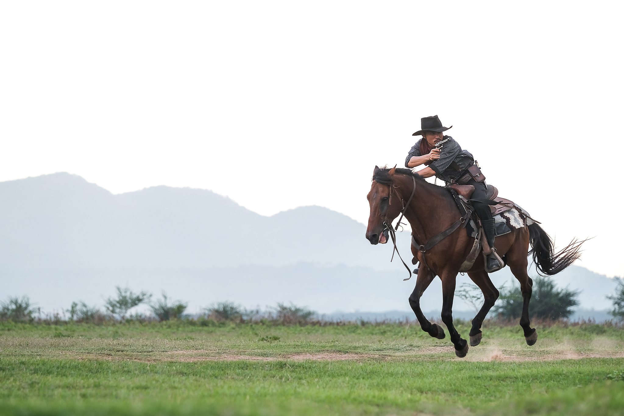 cowboy aiming from gun while riding horse on land