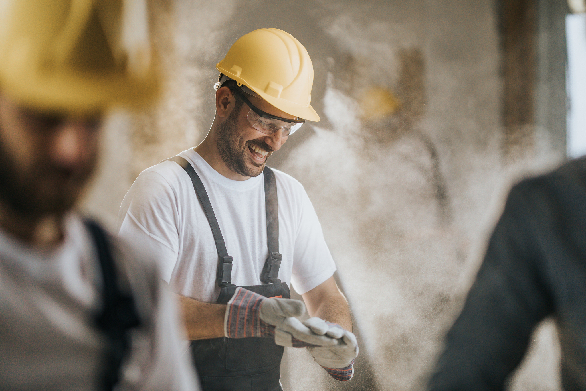 cheerful construction worker cleaning his gloves from sawdust at