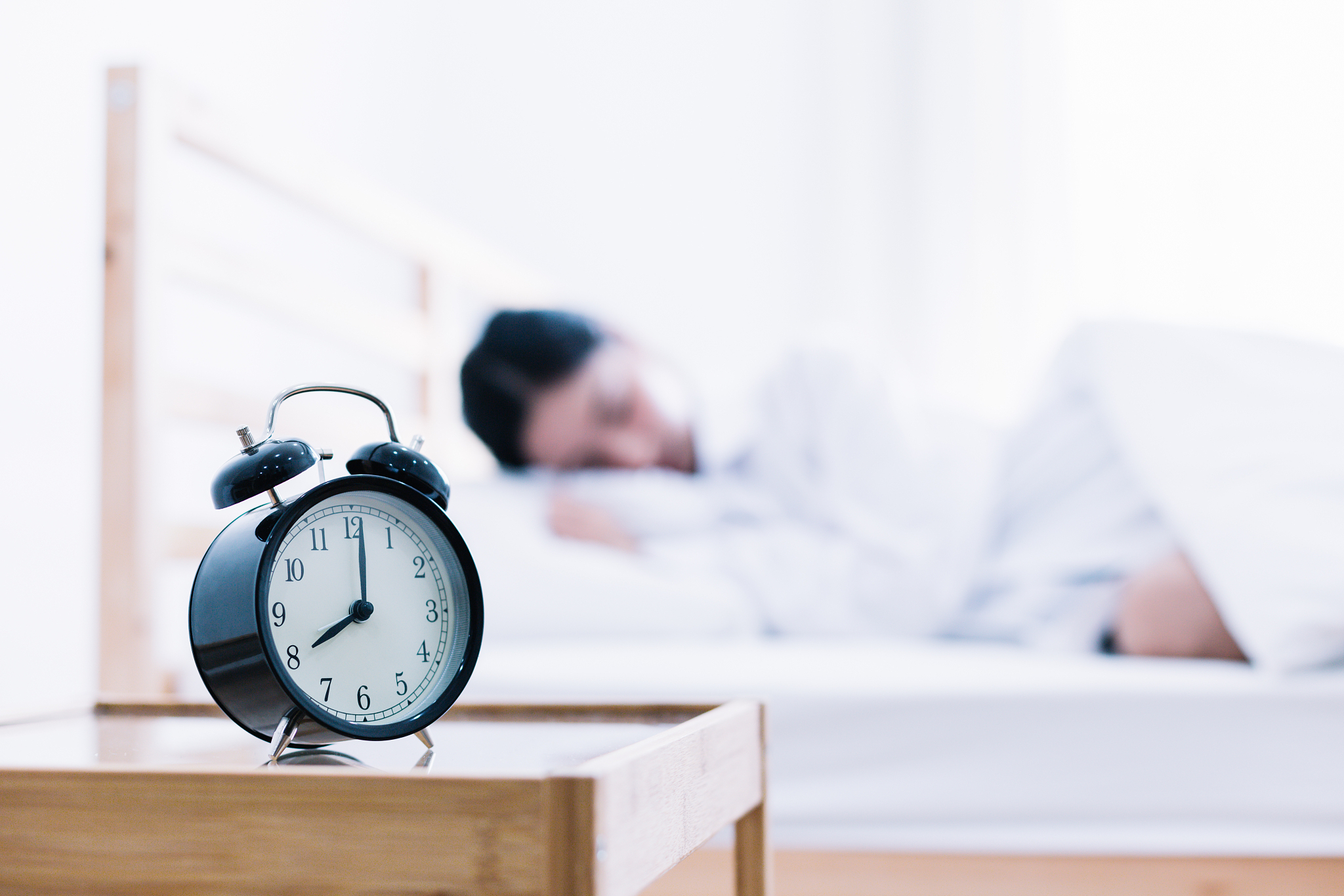 close-up of alarm clock on side table with woman sleeping in bac