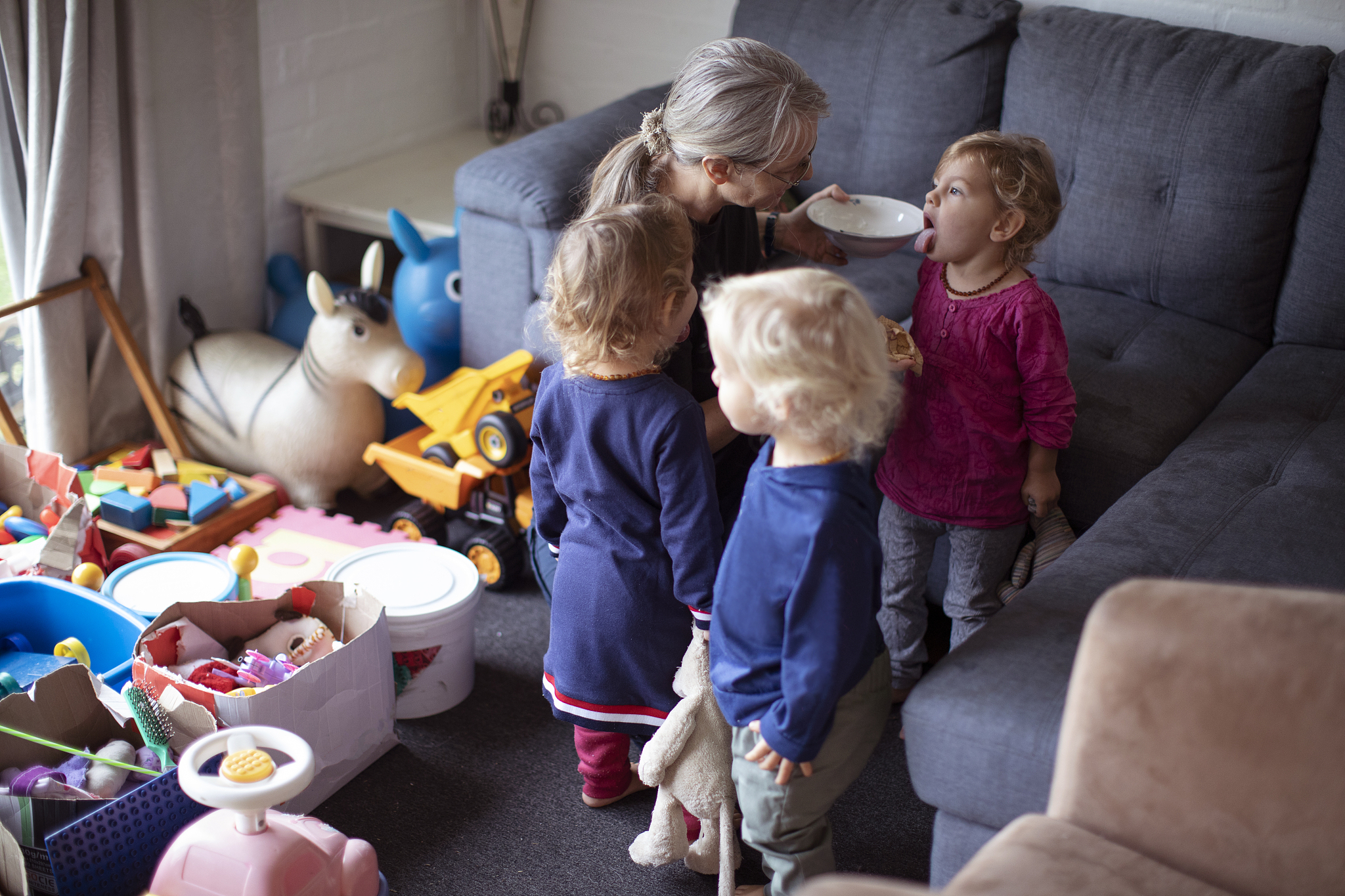 an older mother playing with her young triplets at home.