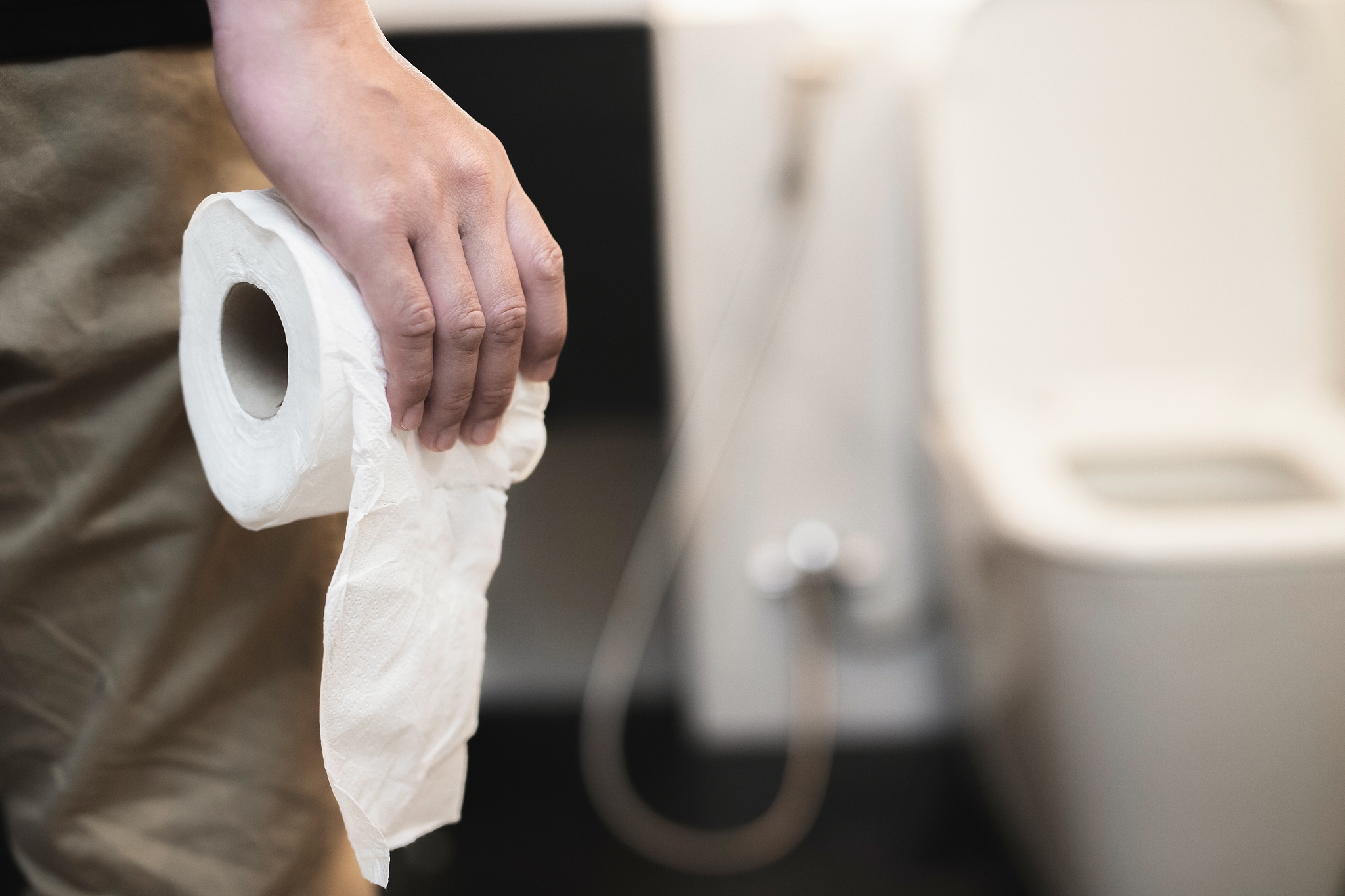 man diarrhea holds toilet paper roll in front of toilet bowl.