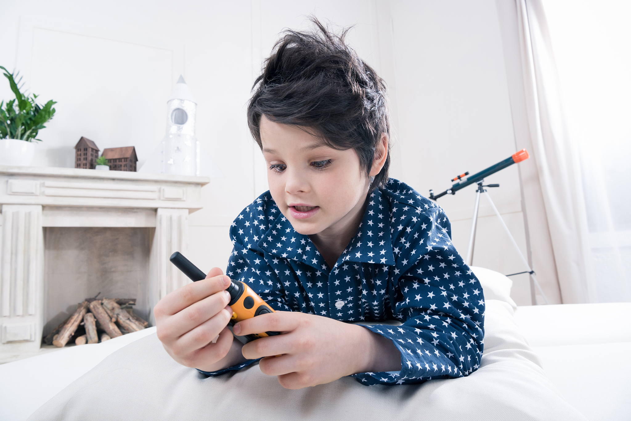 cute little boy in pajamas holding walkie-talkie lying on bed