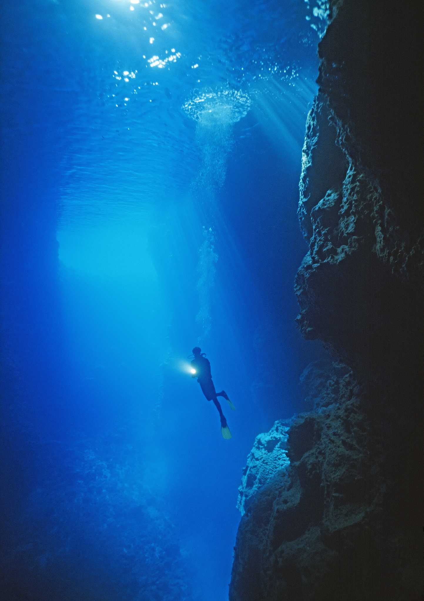 diver with light in large sea cave, underwater