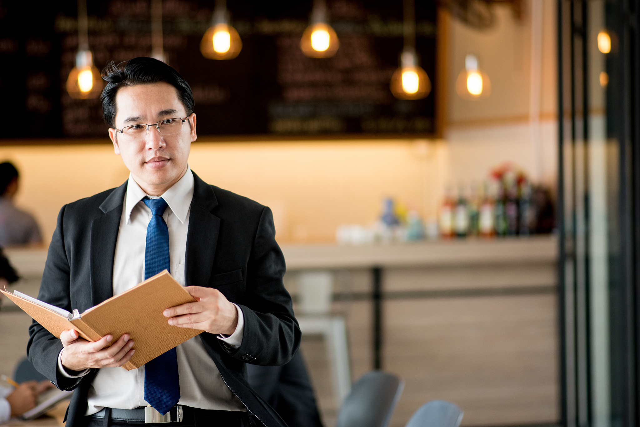 portrait of businessman holding diary while standing in cafe
