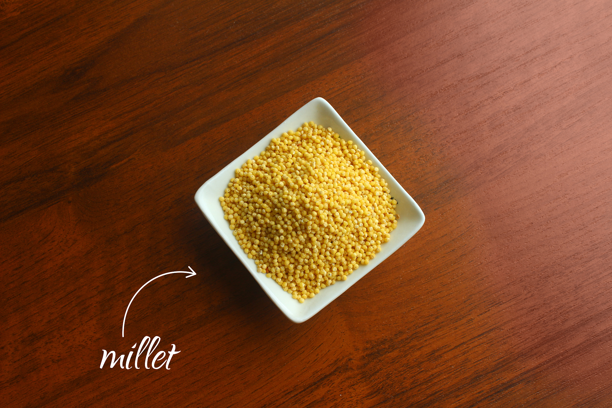 white bowl with grains of yellow dried millet on a wooden table,