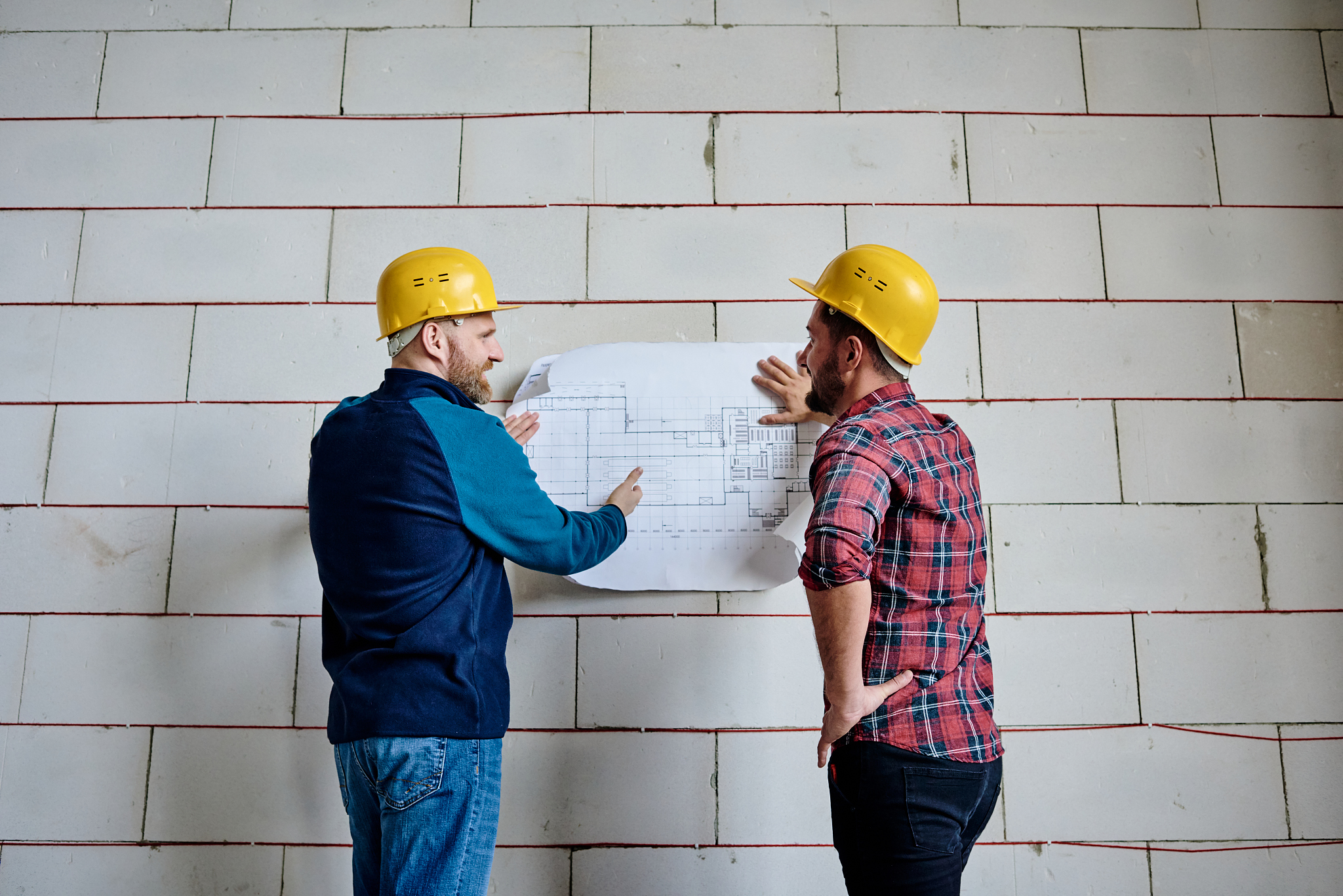 two successful builders in protective helmets discussing bluepri
