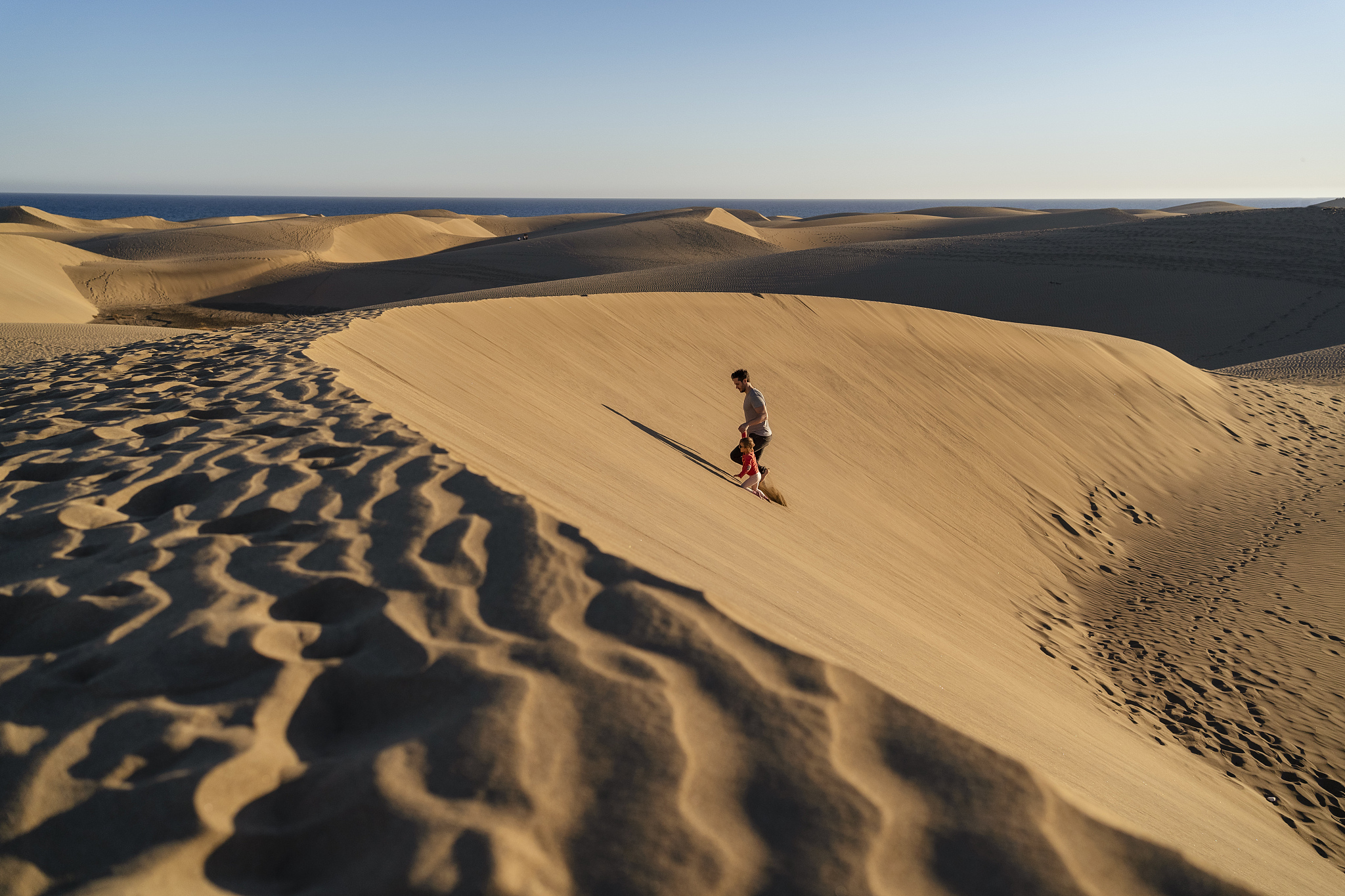 father and daughter walking up sand dune, gran canaria, spain