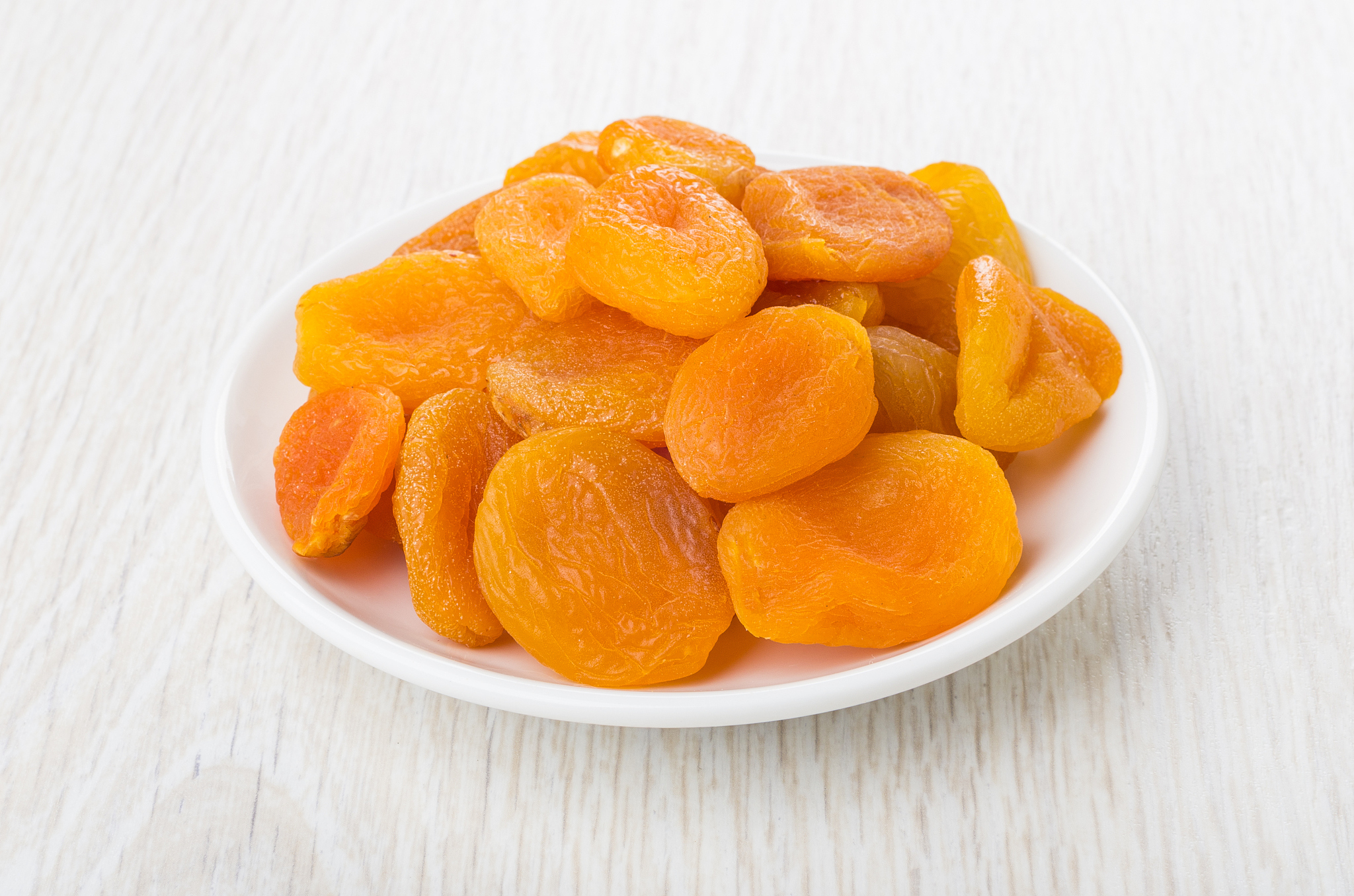 dried apricots in white saucer on wooden table