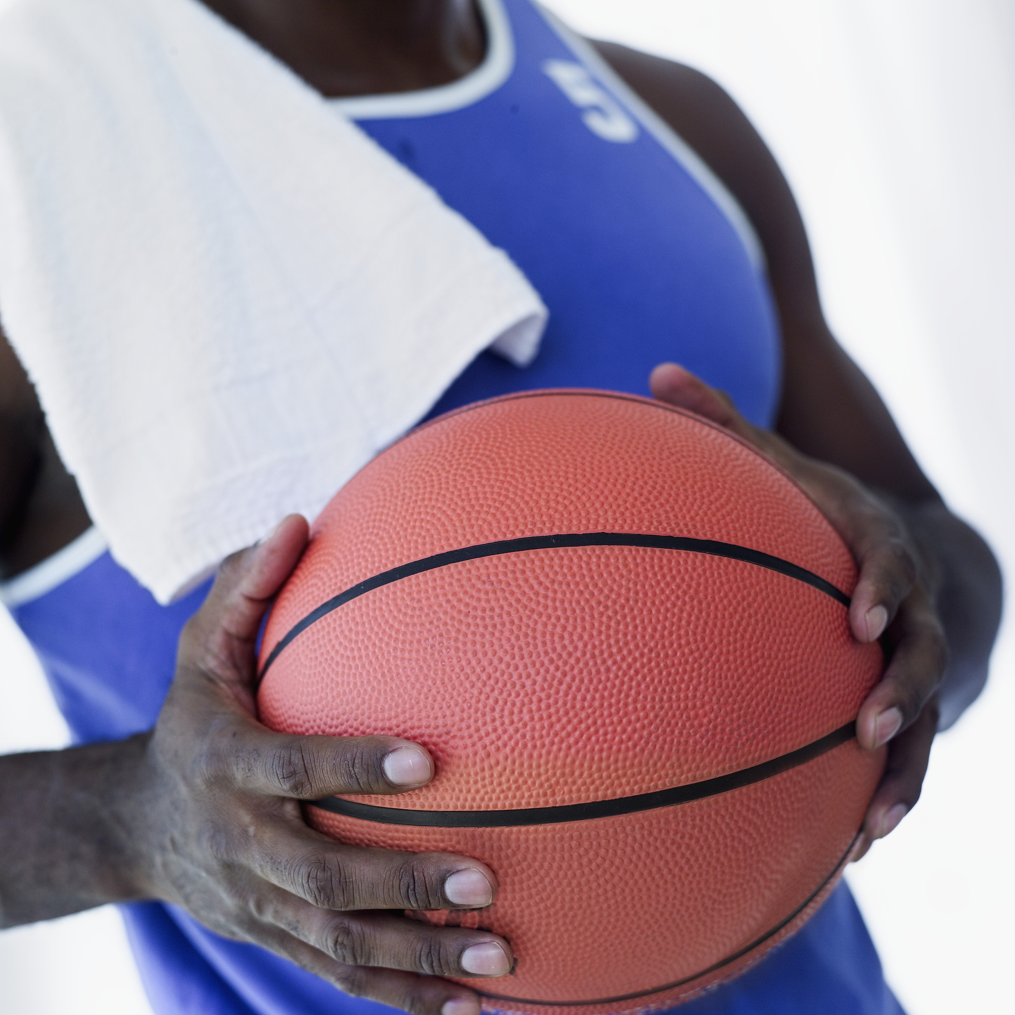young man standing holding a basketball with a towel on his shou