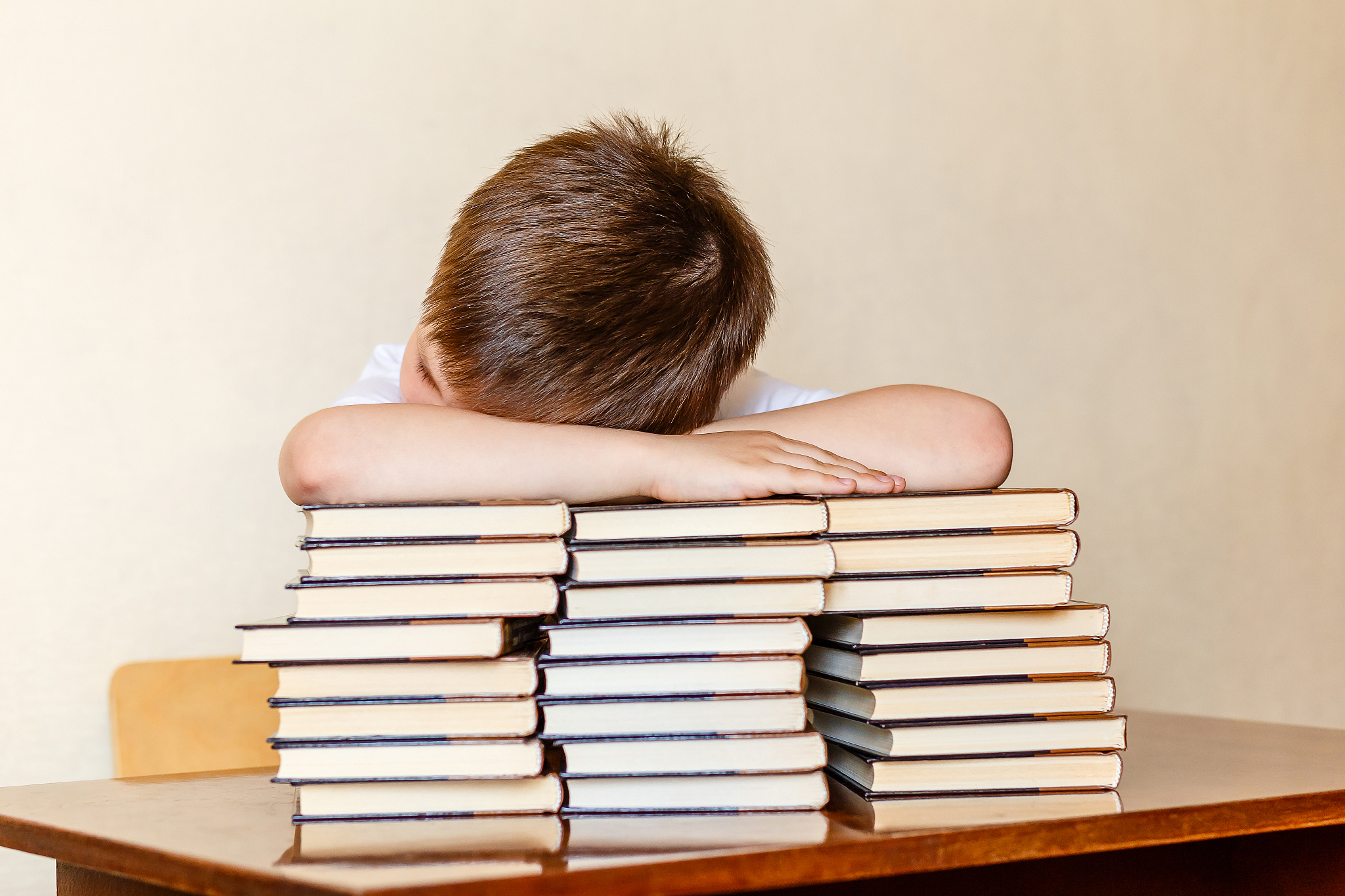 the child sits at the table, putting his head on the books.