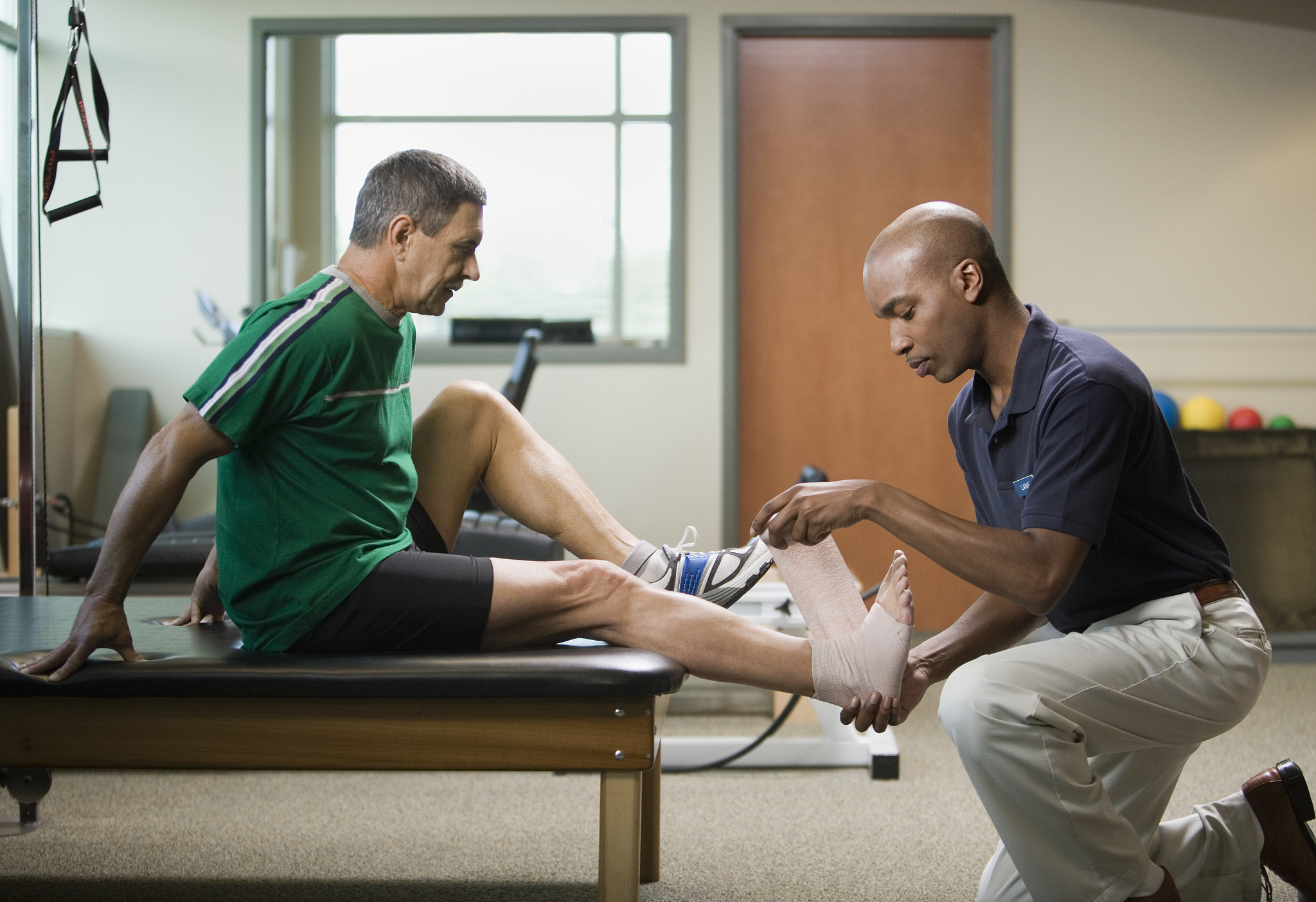 physical therapist wrapping mature man's foot in bandage, side v