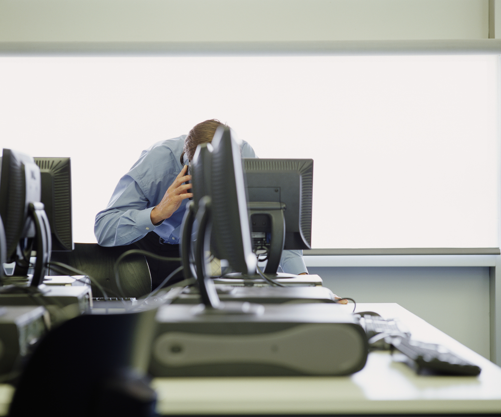 businessman using phone behind computer, face obscured by screen