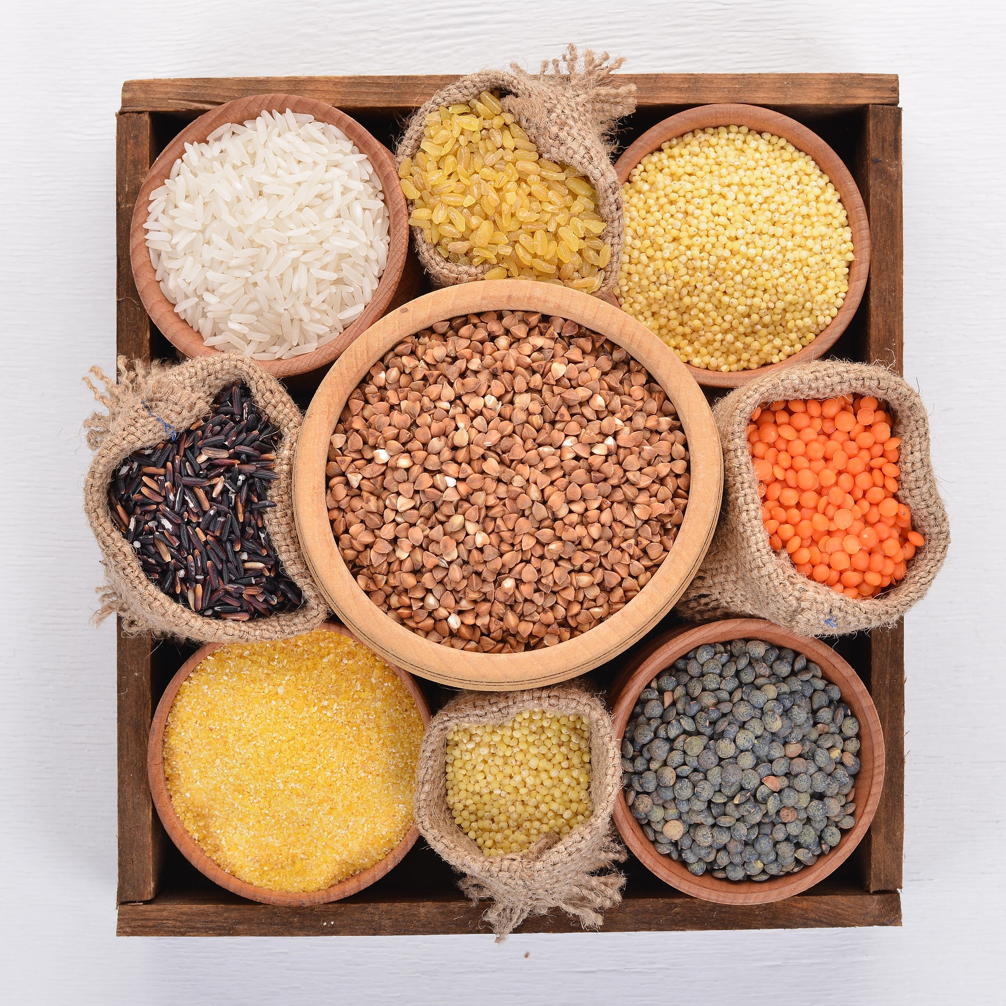a set of cereals and grains in a wooden basket on a wooden backg