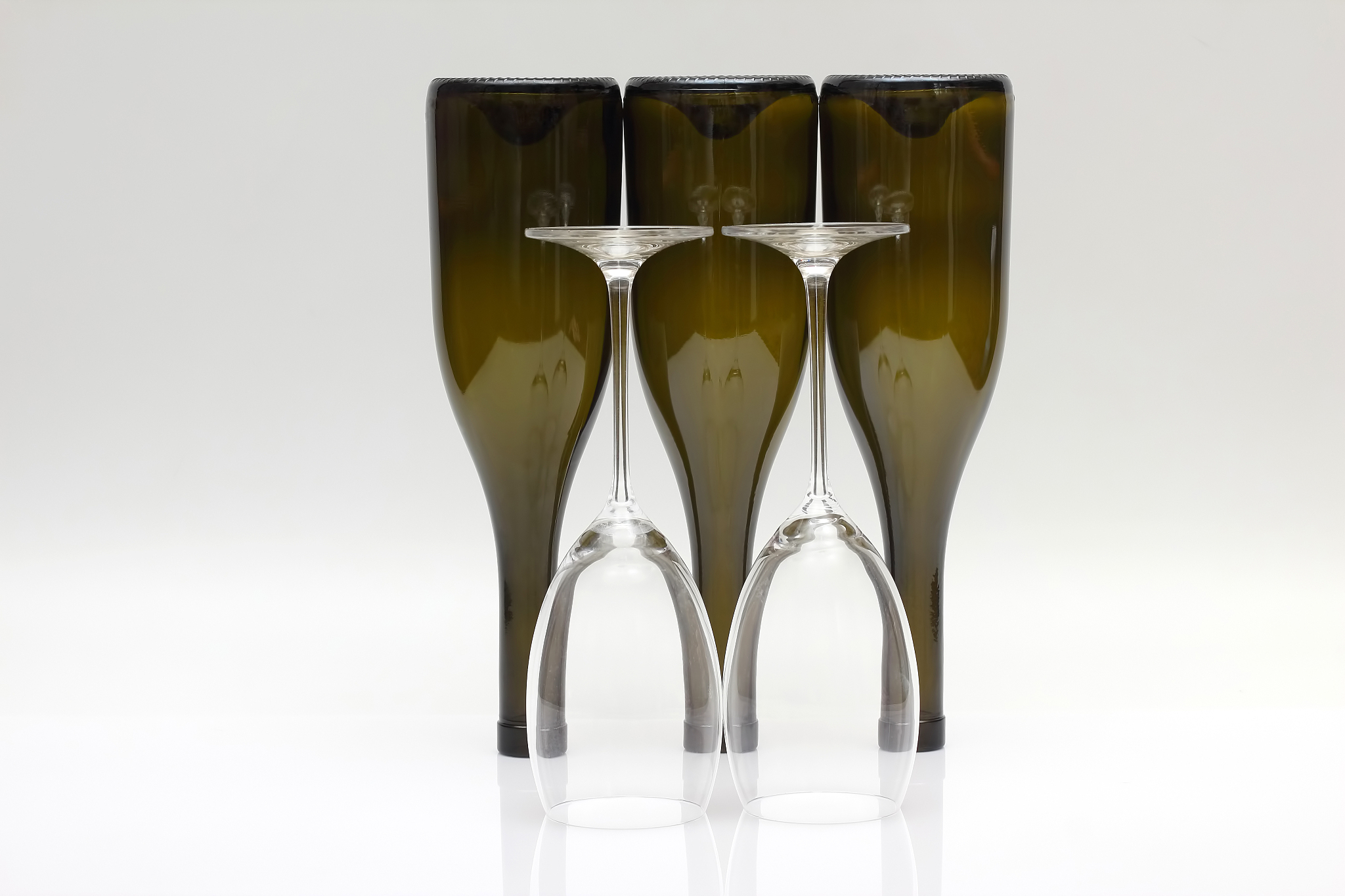 three empty upturned wine bottles and two glasses on a white bac