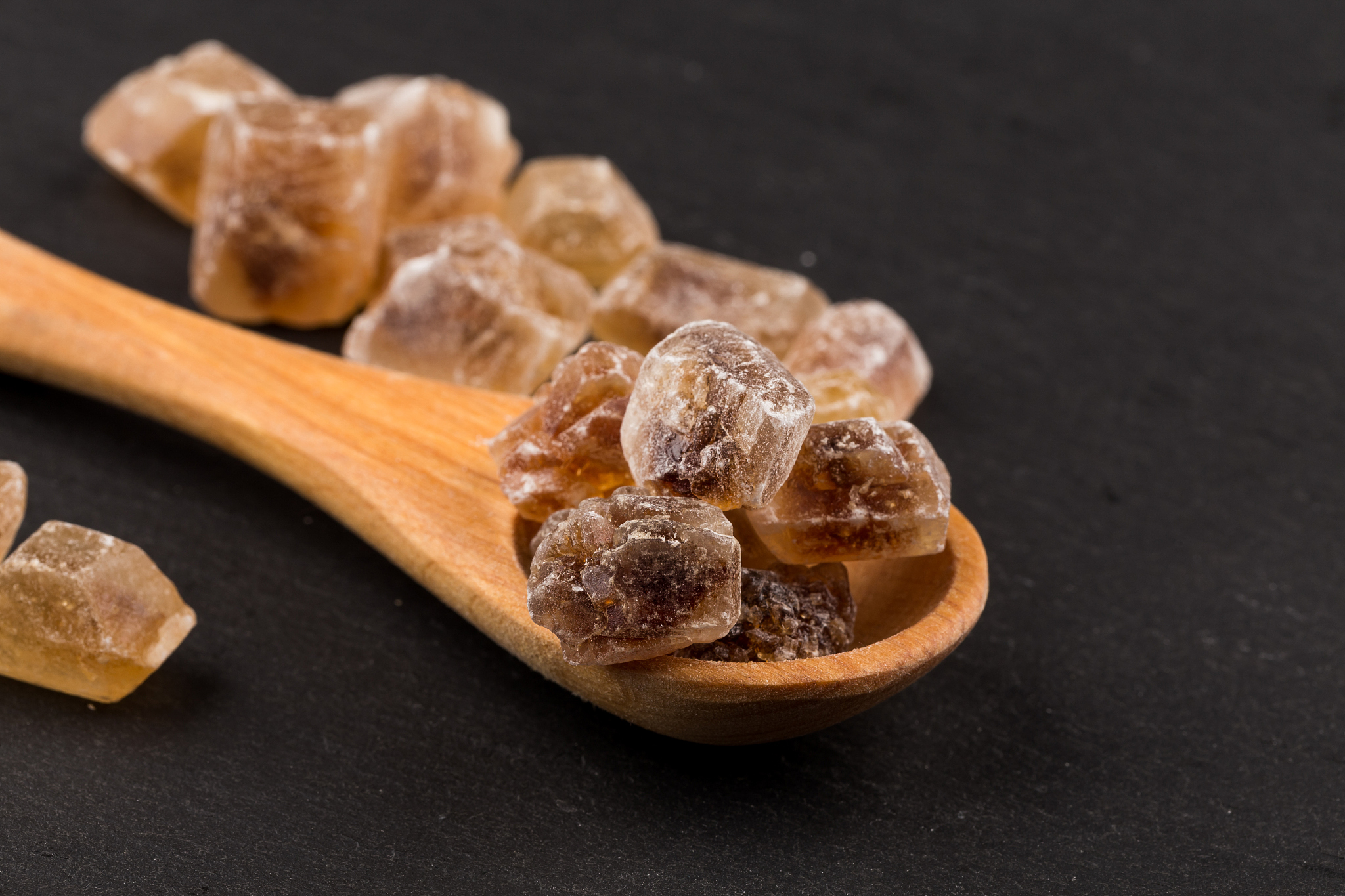 caramelized candy brown sugar in wooden spoon on a dark stone bo