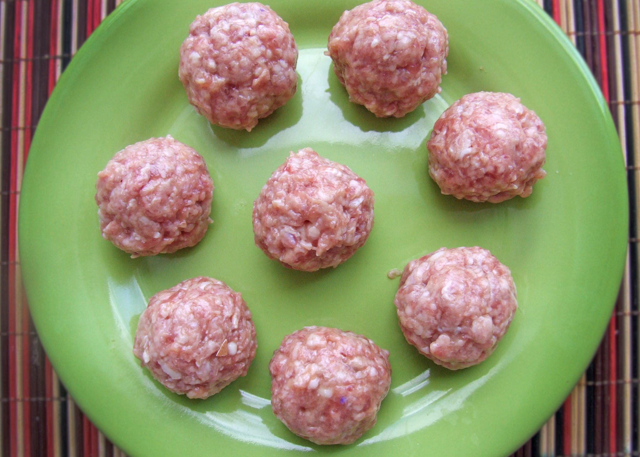 raw meatballs with rice and onions on a green plate.