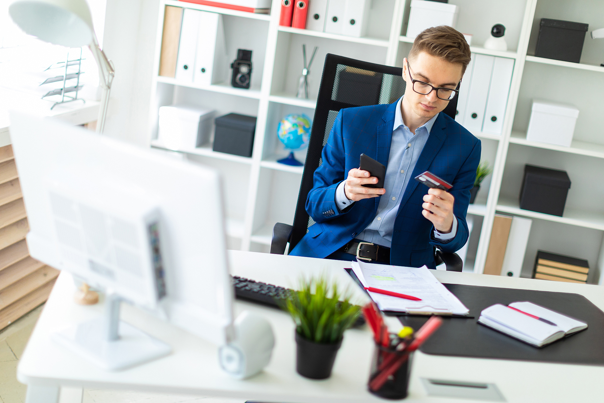 a young man sits at a table in the office and holds a bank card 