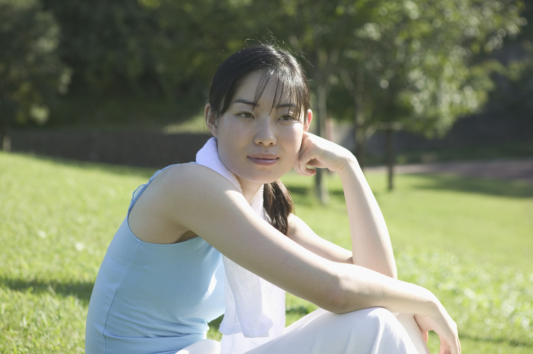 young woman sitting in park, resting head on hand, smiling