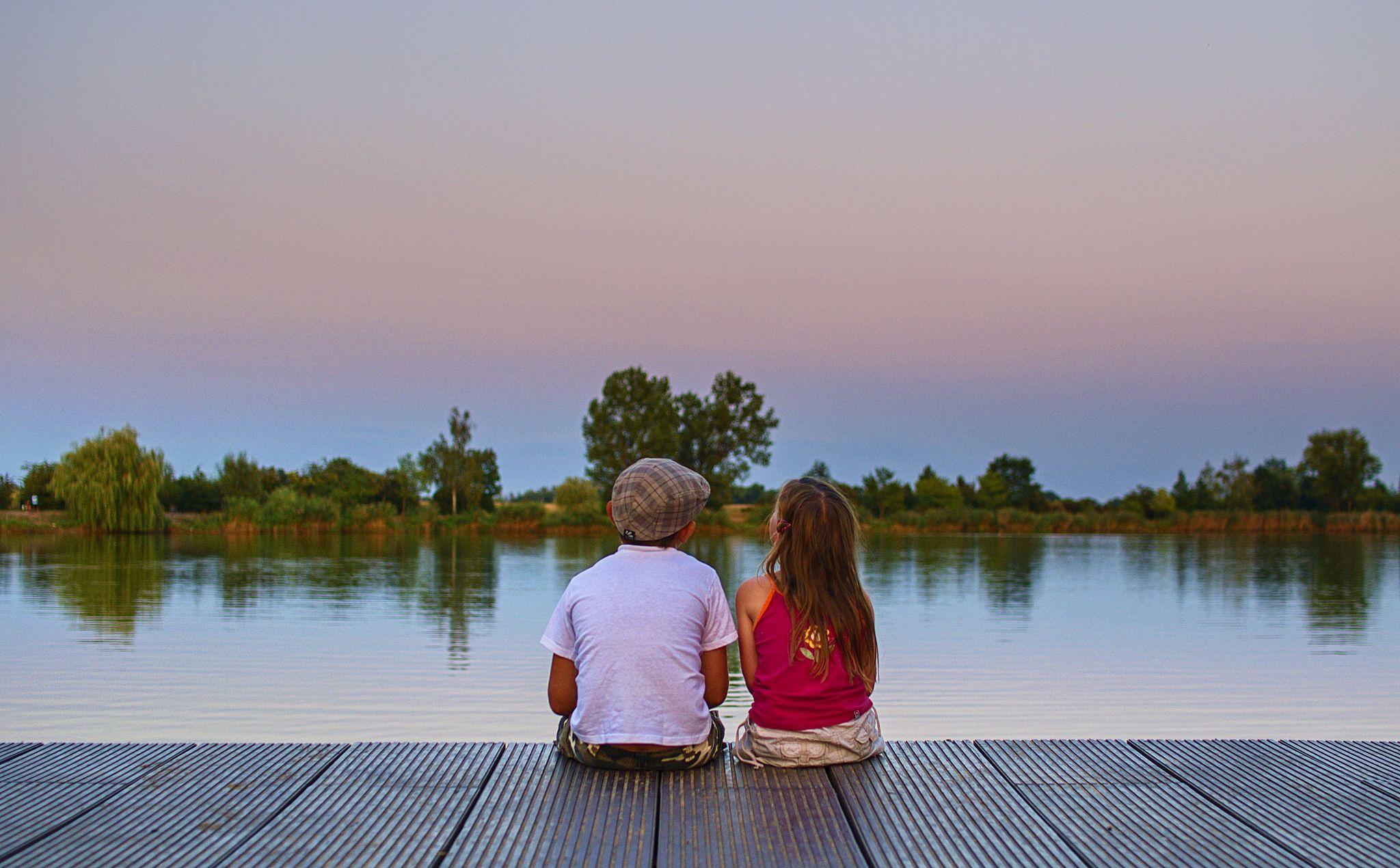 boy with flat cap and little girl are sitting on pier. boy and g