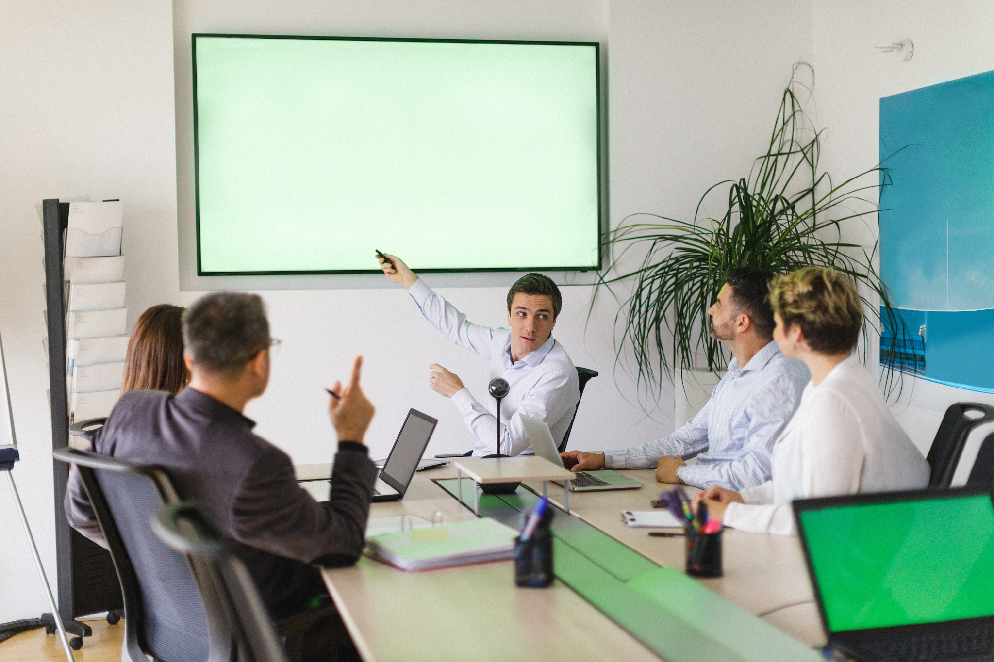 man pointing with remote at screen, turning to colleagues