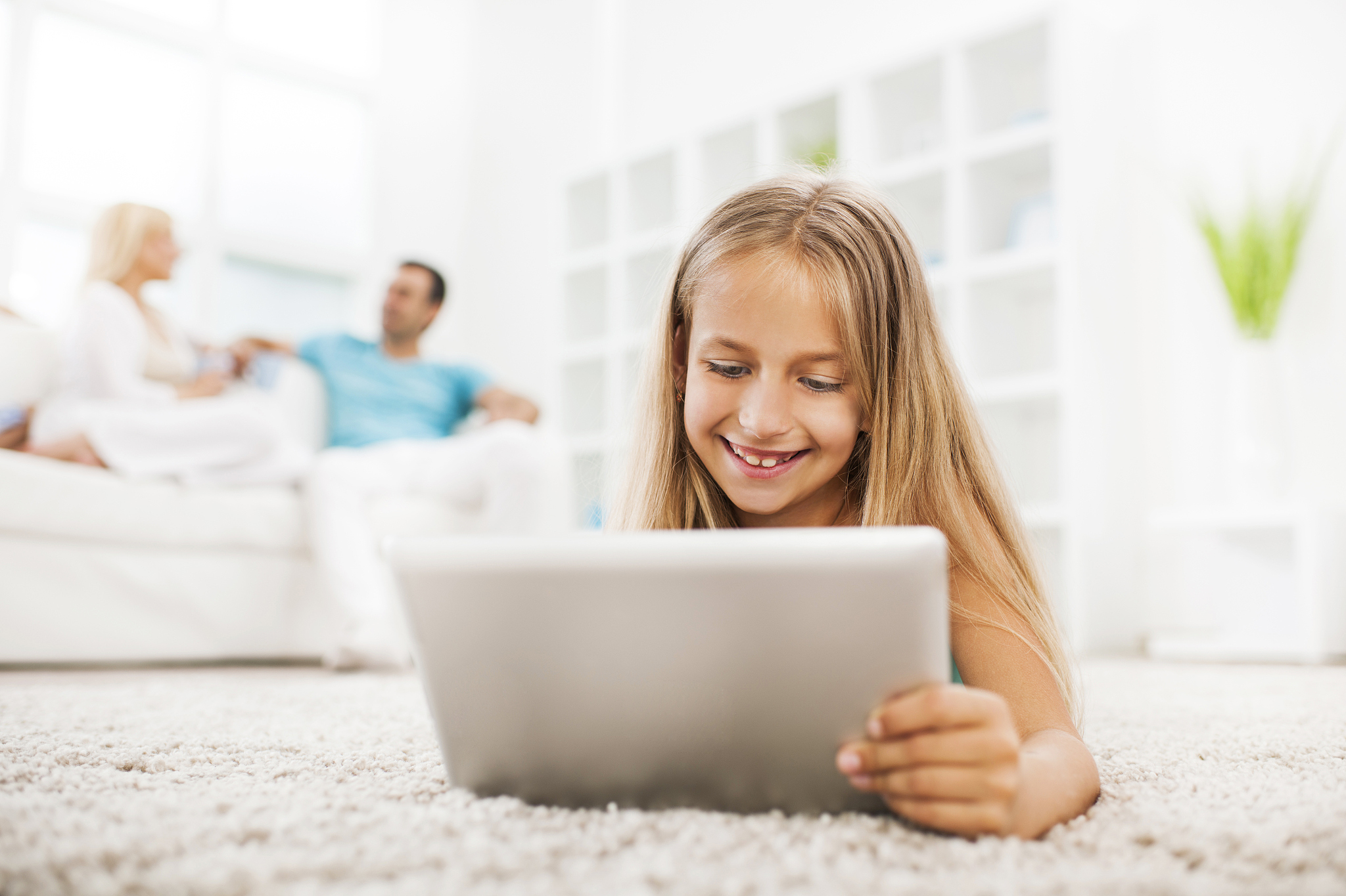 smiling little girl lying on the carpet and using touchpad.
