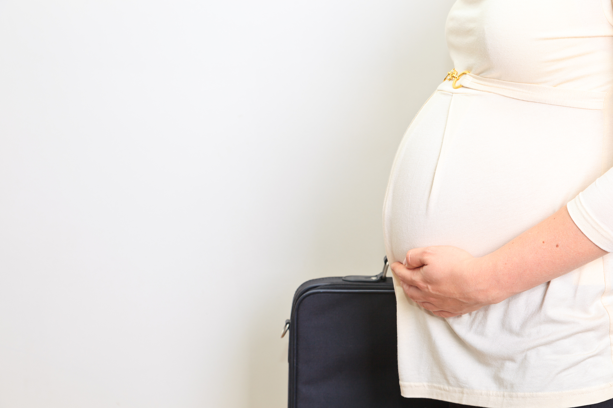 pregnant businesswoman standing with briefcase against white bac