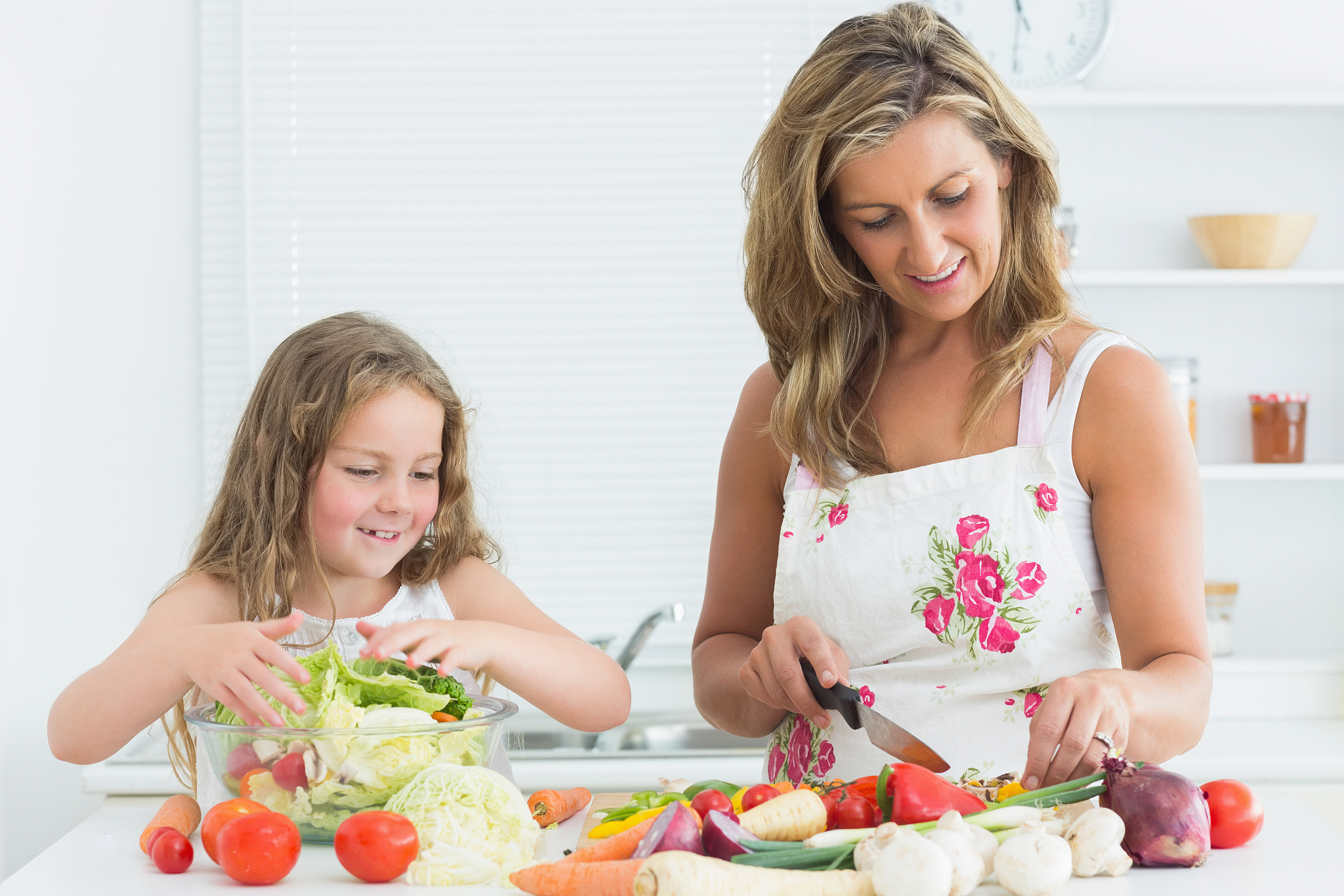 smiling mother and daughter preparing vegetable salad
