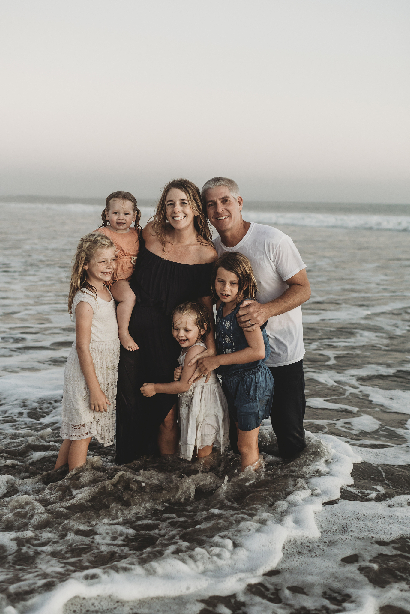 portait of young family with wet hair standing in ocean at sunse