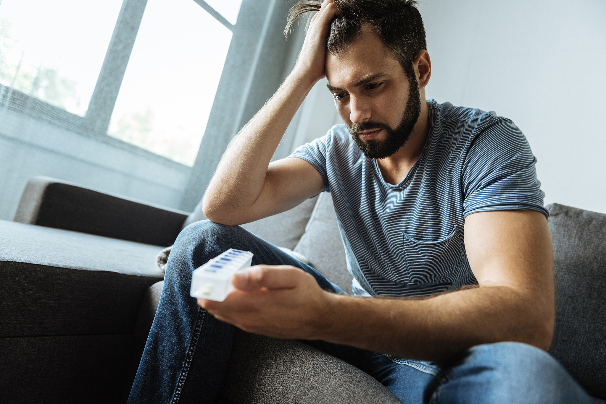 depressed gloomy man holding a pill organizer