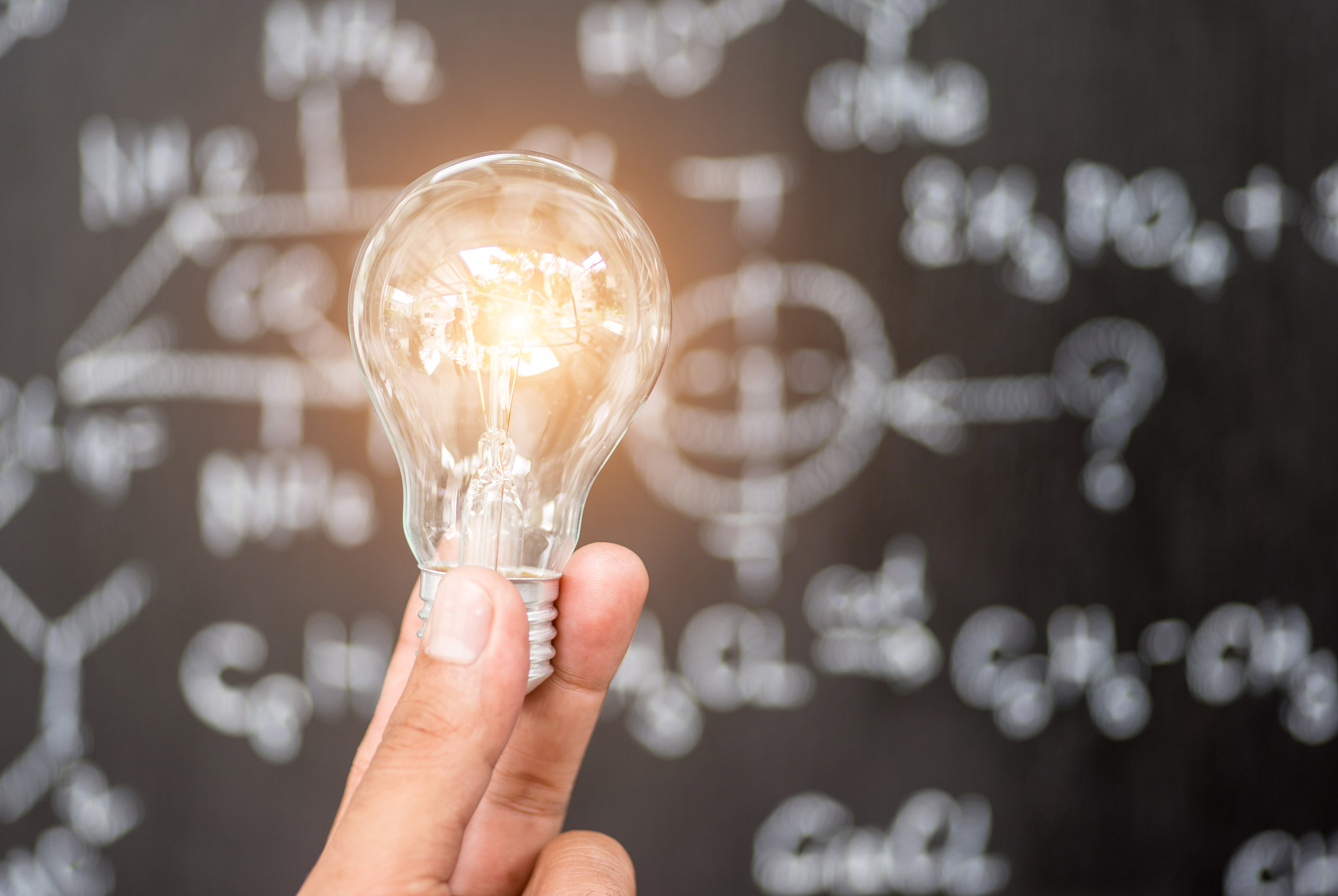 hand holding light bulb on blackboard background