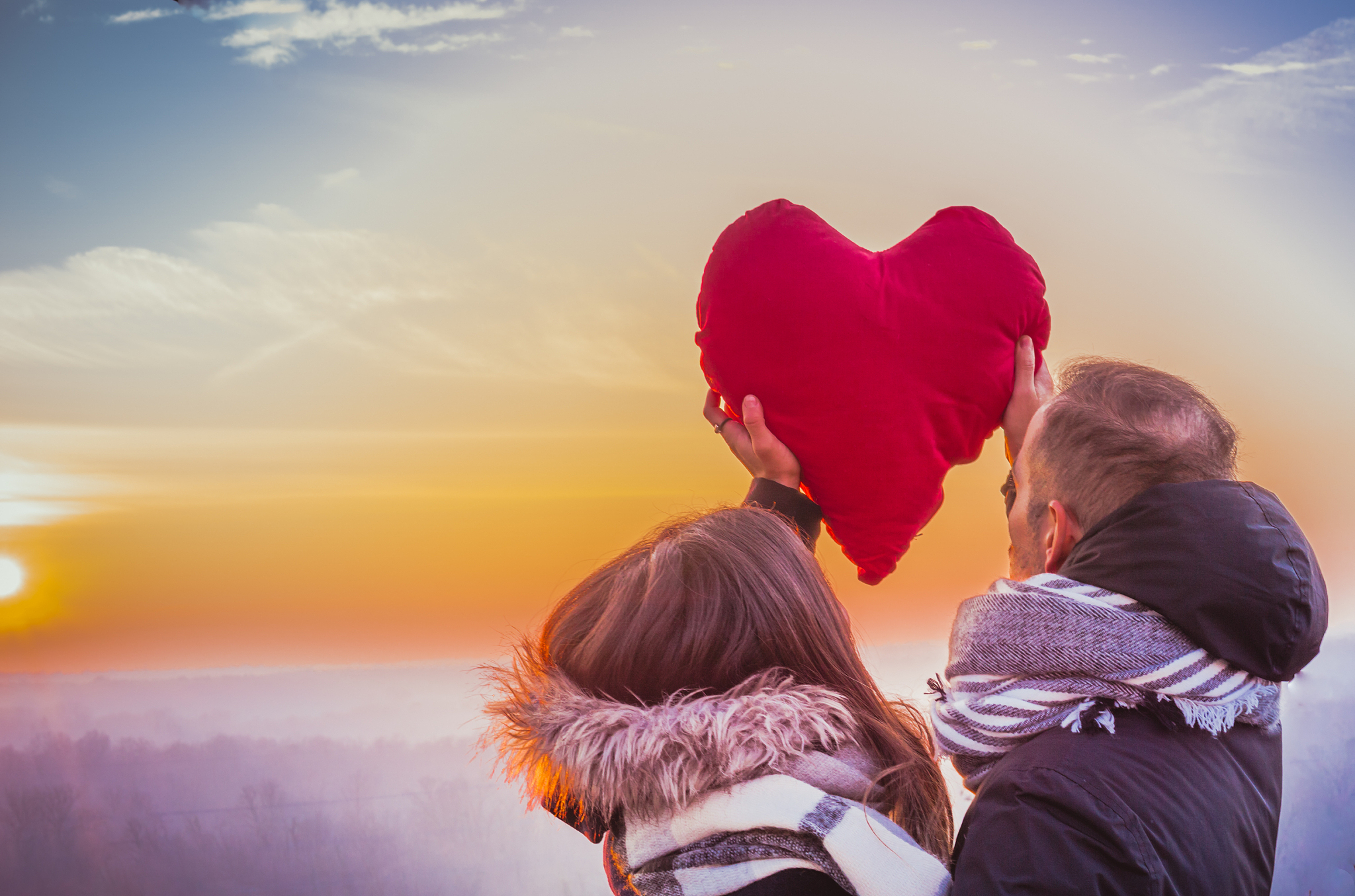 young couple holding red heart shape cushion against sky during 