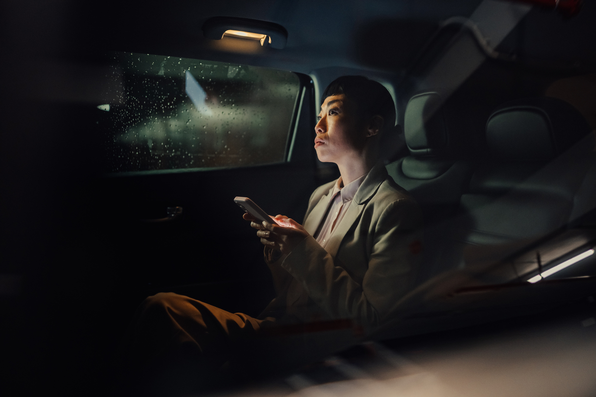 雨夜通勤,一位职业女性在汽车后座使用智能手机,若有
