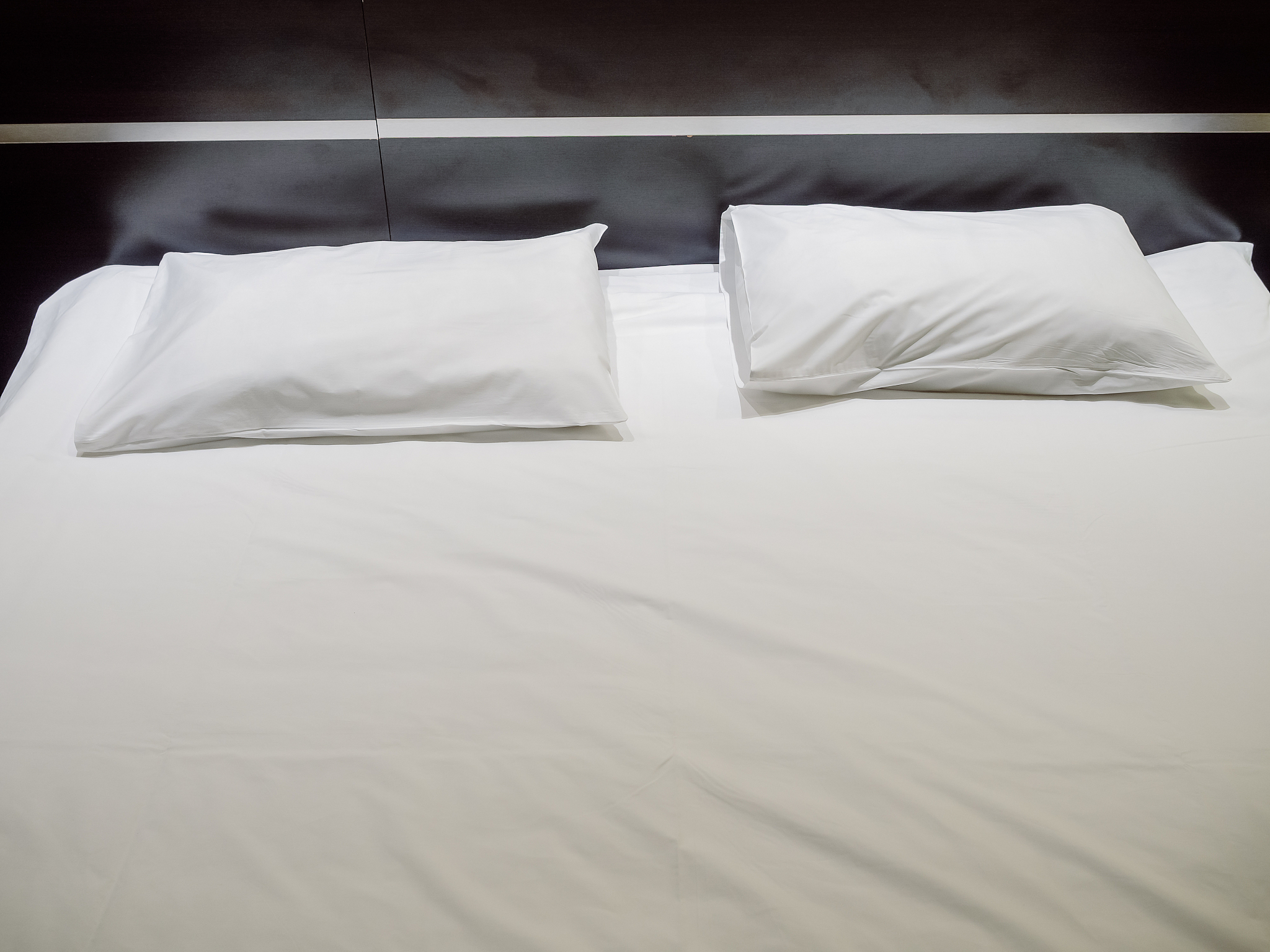 two rectangular pillows in white pillowcases lie on a white shee