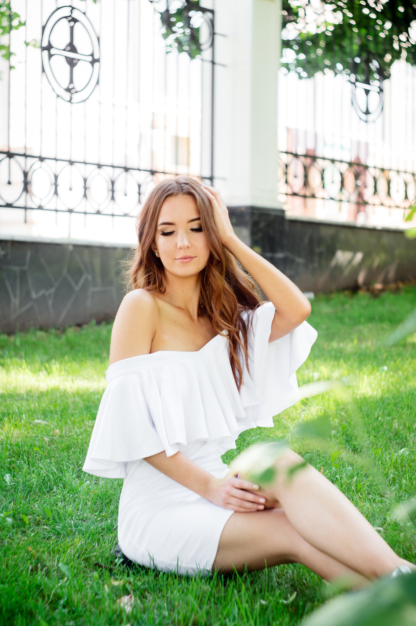 a young woman in a white dress sitting in the park on the road.