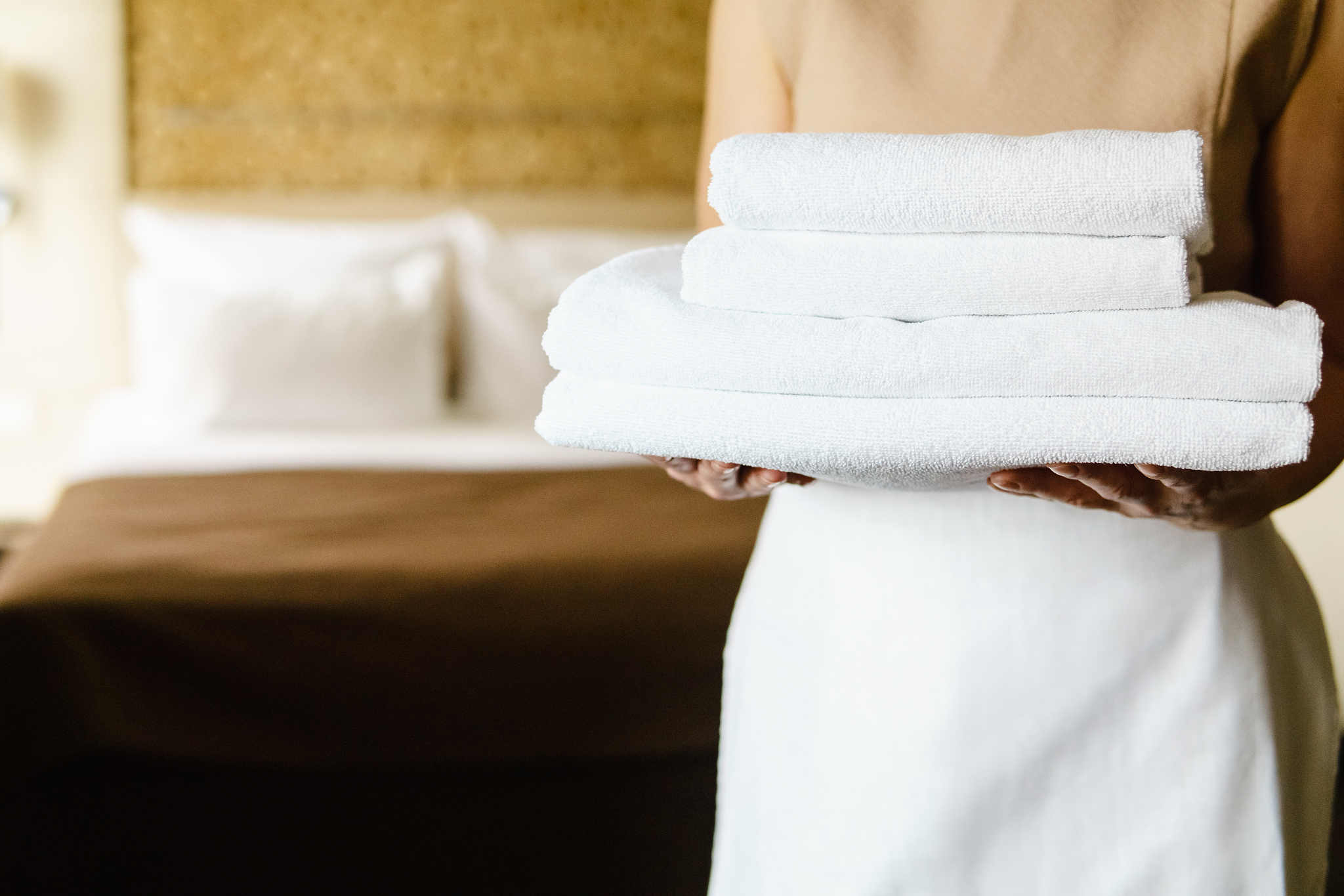 maid holds clean towels while standing in the hotel room.