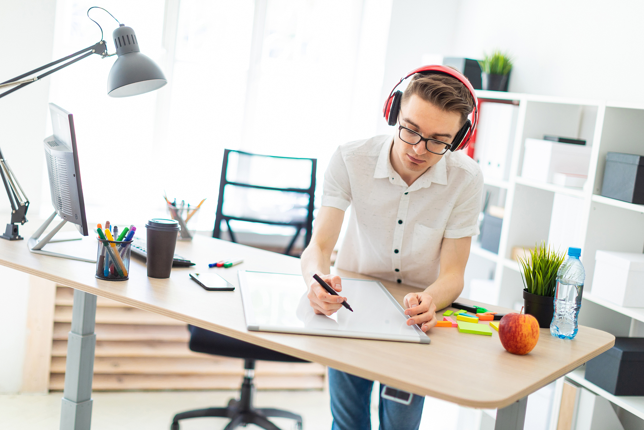 a young man with glasses and headphones draws a marker on the ma